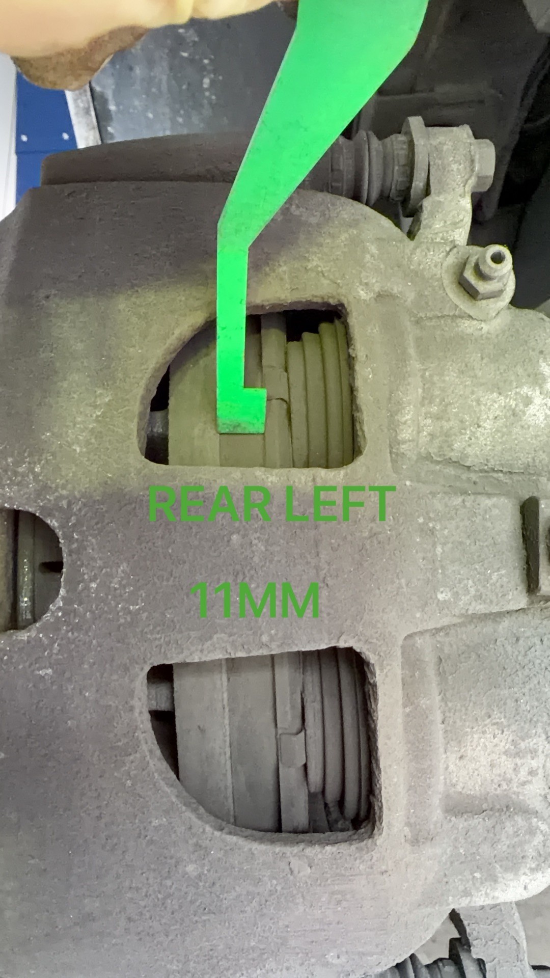 Rear left brake caliper with a green pad gauge in the inspection window, marked 11 mm