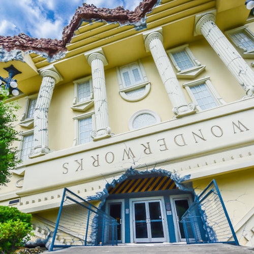 An upside-down building labeled "WonderWorks," featuring classical columns and a cracked roof design beneath a blue sky with clouds.