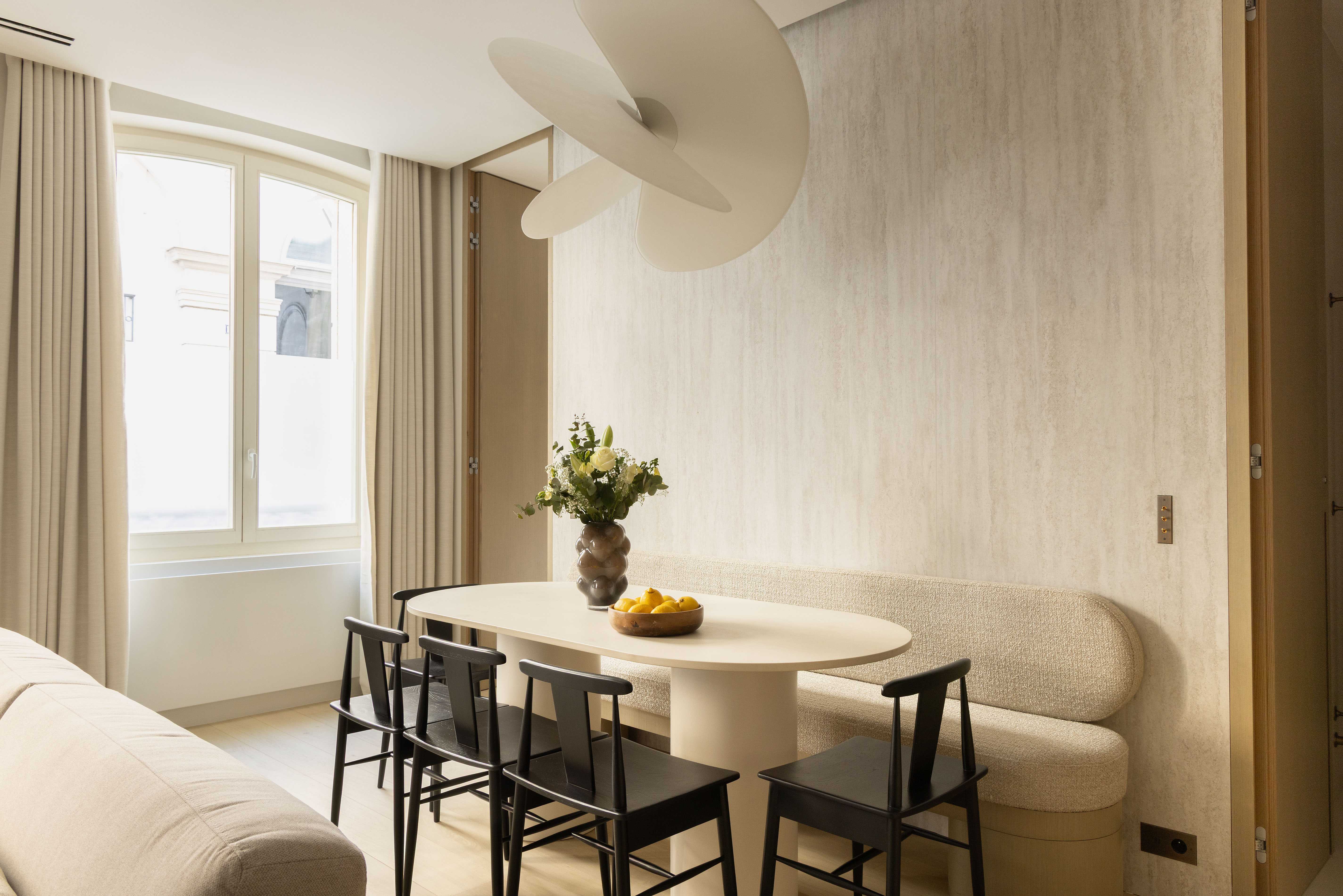 Coin repas avec table ovale, banquette arrondie beige, chaises noires et suspension blanche sculpturale