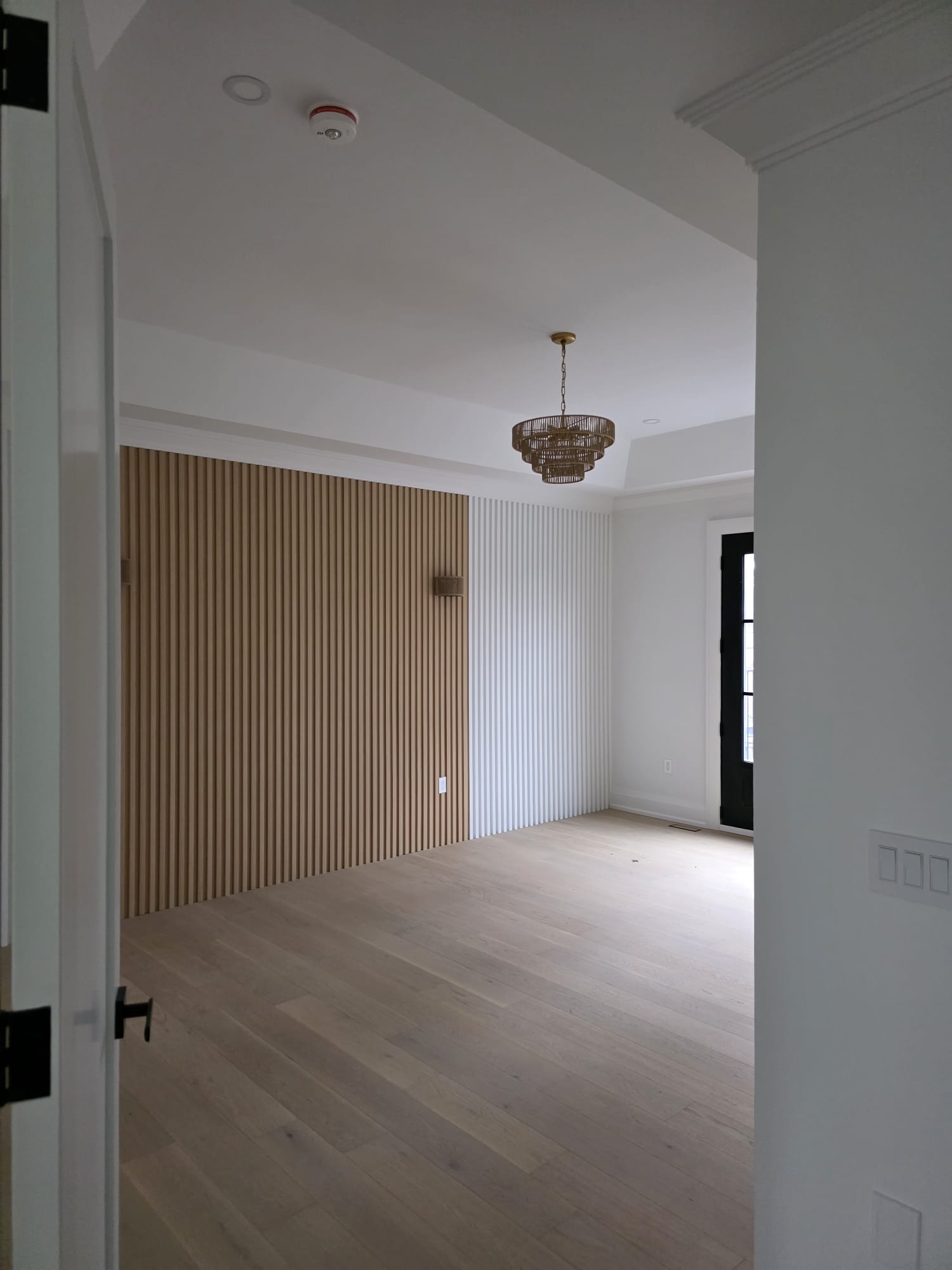 Spacious modern apartment with a kitchen island, black chairs, and stainless steel appliances. A cozy living area with armchairs and plants in the background.