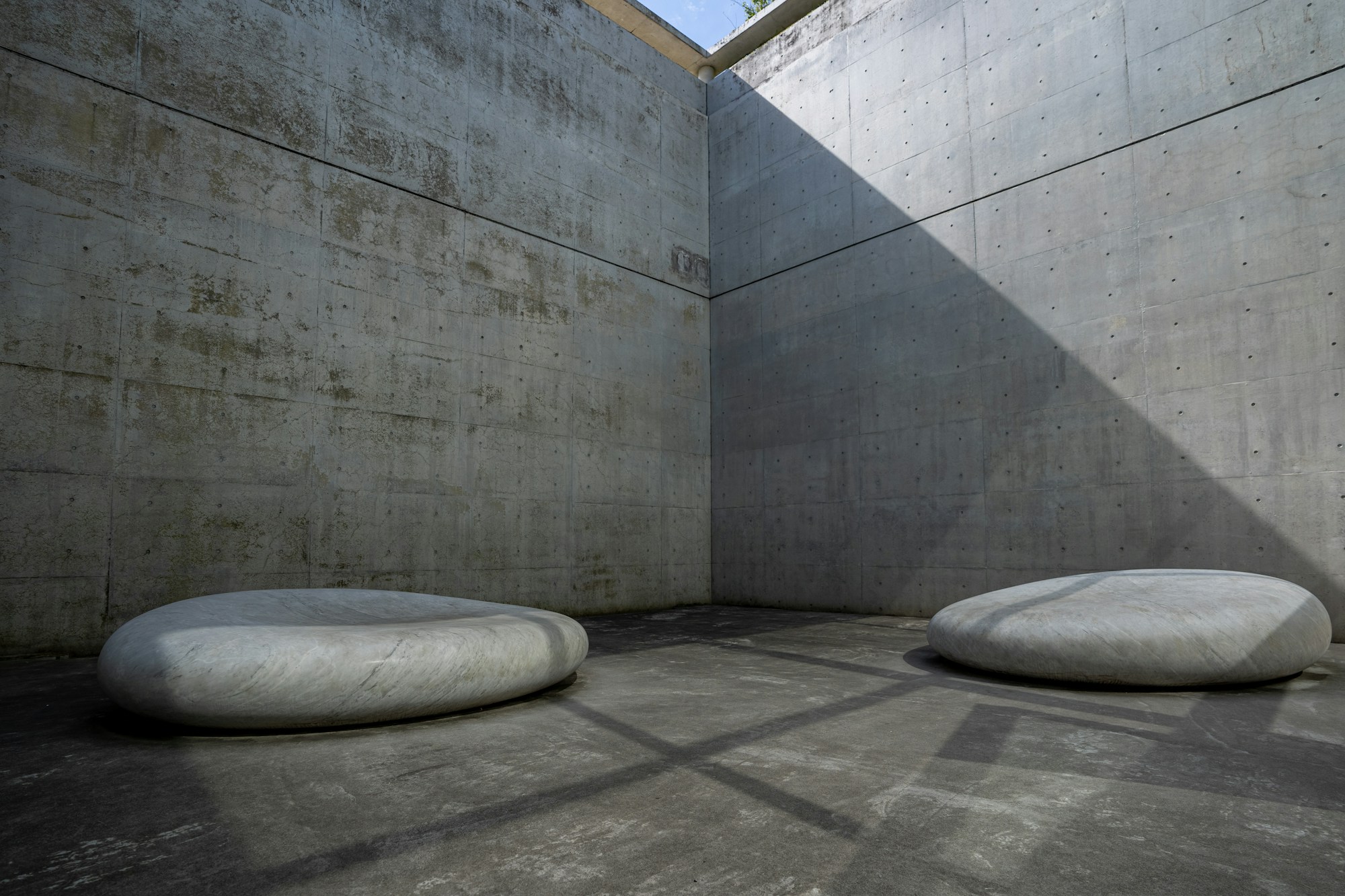 Walled concrete courtyard with two smooth stone seats in soft shadow