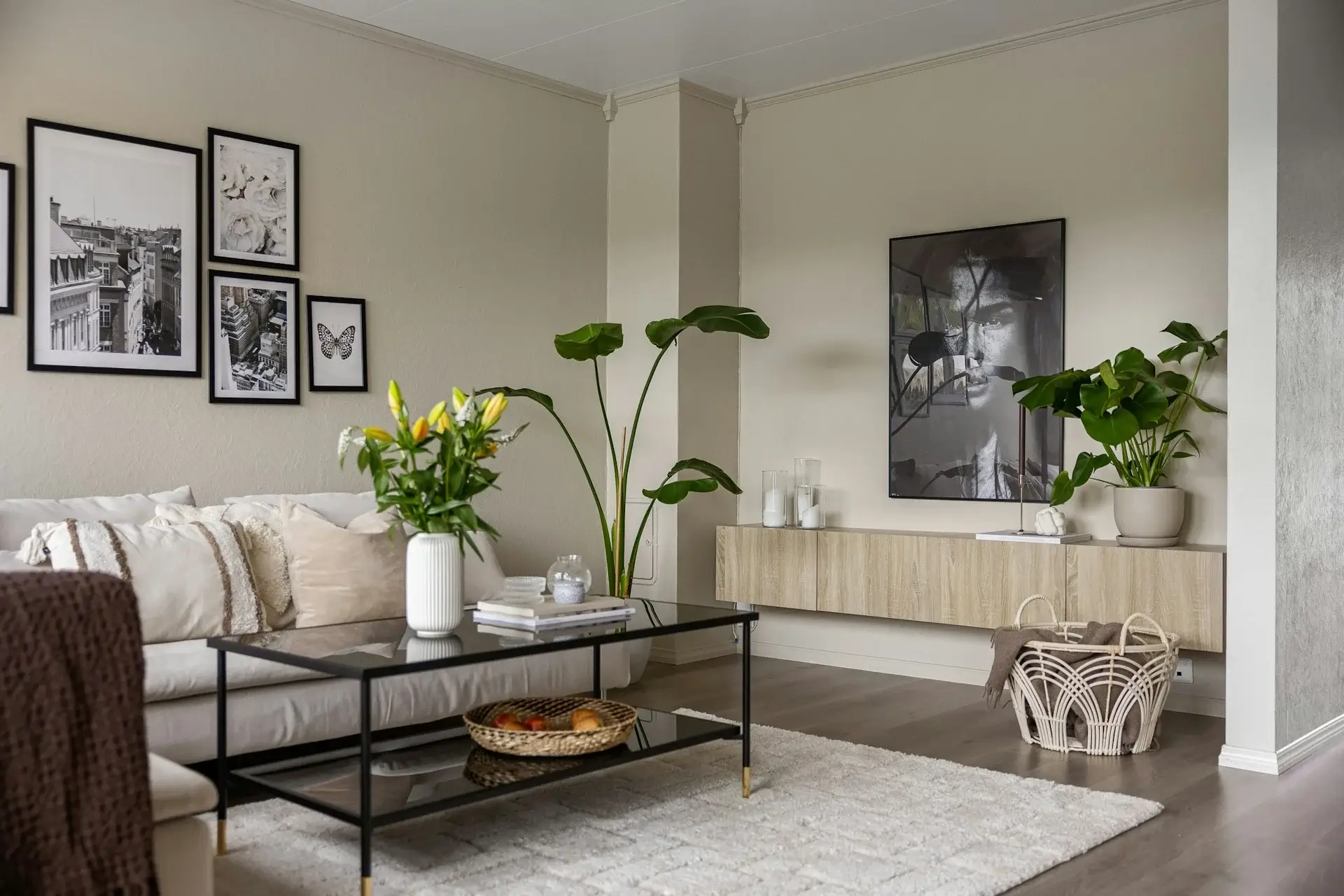 Neutral living room with beige sofa, glass coffee table, wall art, and indoor plants.