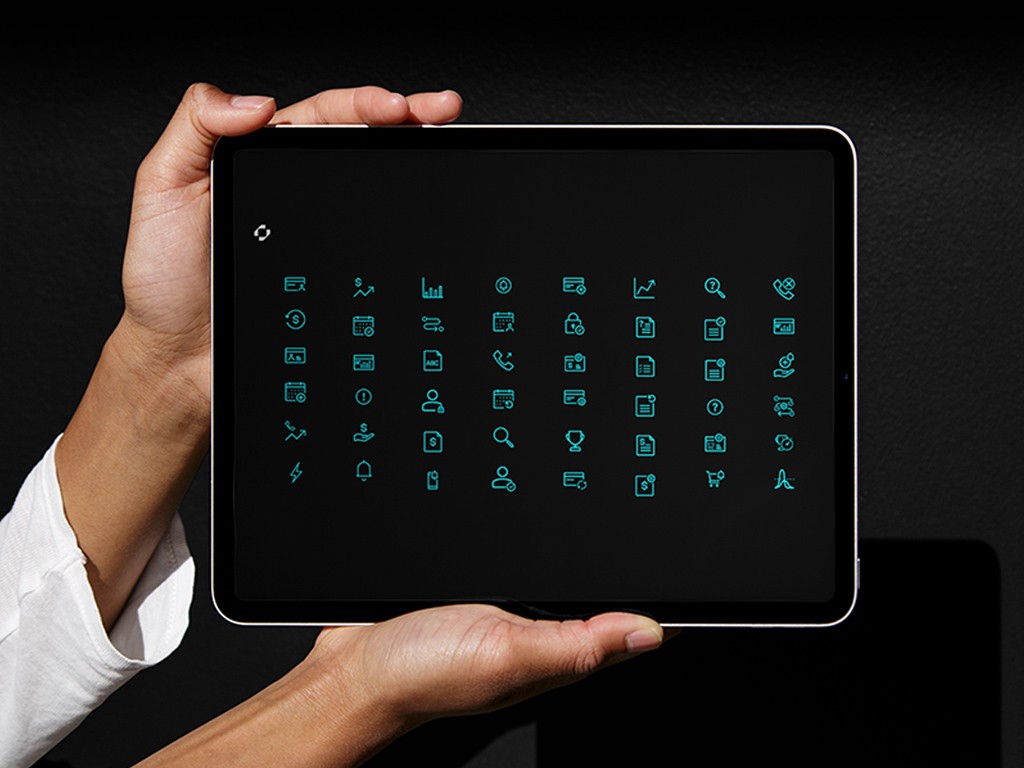 Hands holding a tablet displaying a custom icon system developed for Replicant, featuring a grid of minimal cyan interface and communication icons against a dark background.