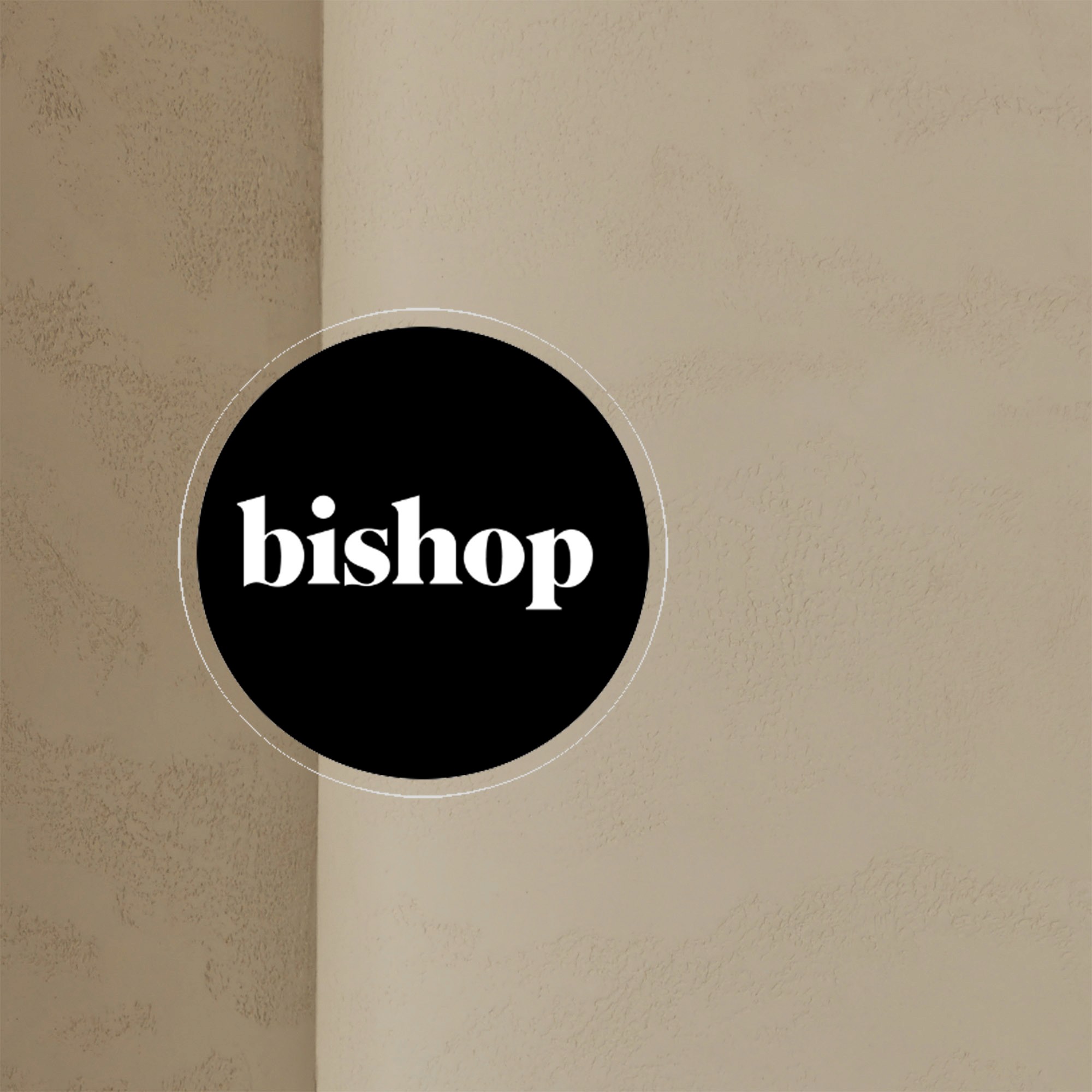 "bishop" logo in white text on a black circle over a textured plaster wall
