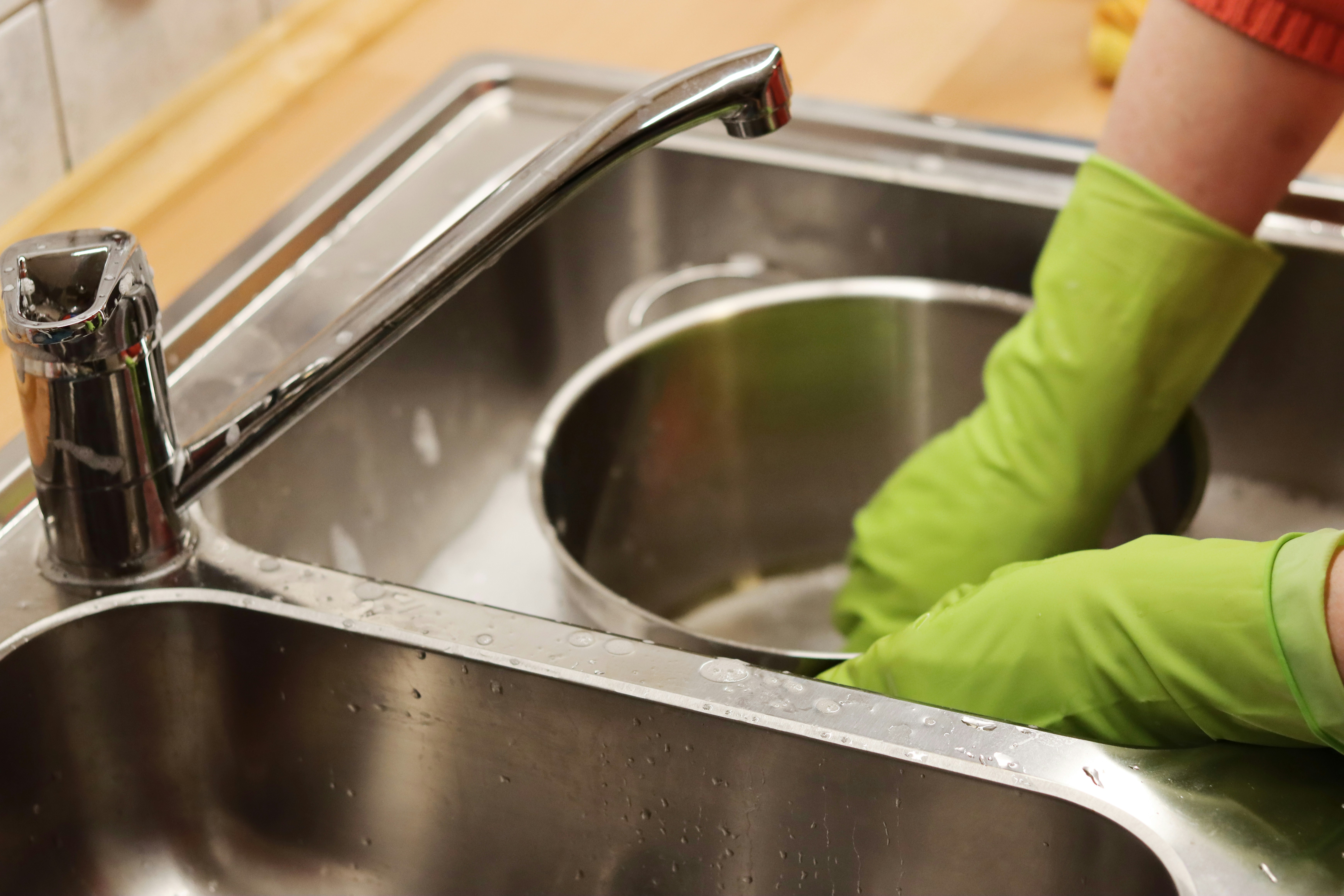 person in green long gloves washing stainless steel sink