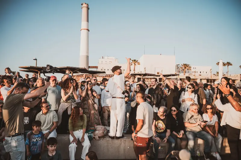 קהל בהופעה חיה בשקיעה מול תחנת הכוח ברידינג תל אביב, צילום אמנותי של הצלמת שירי עציץ Shiriz המתעד רגעי קהילה ומוזיקה תחת כיפת השמיים.