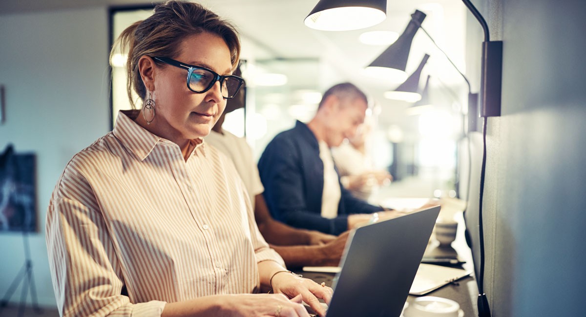 Woman focused on her laptop in a shared workspace, illustrating individual contribution to team goals