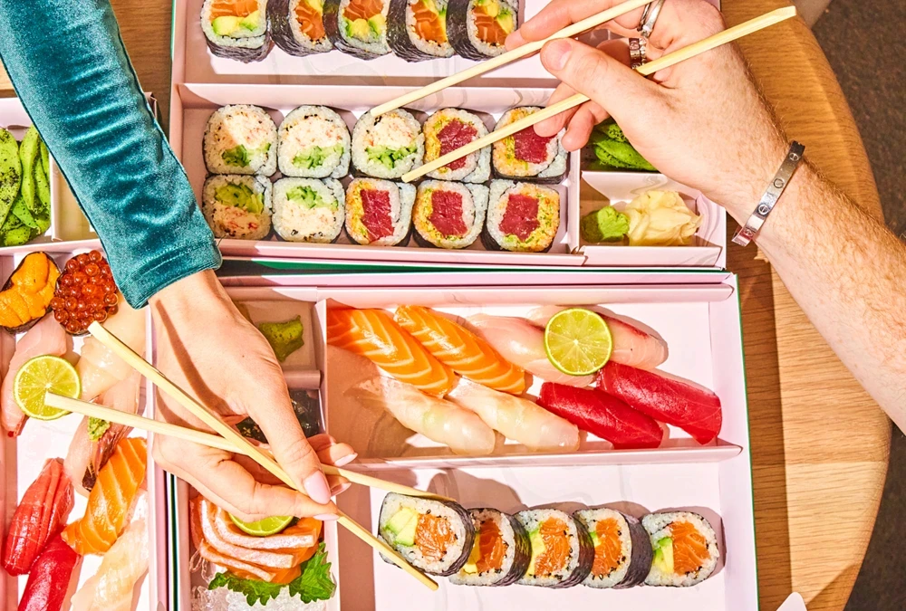 Hands sharing sushi from Bento by Point Seven boxes