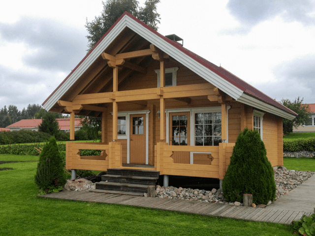 Ulkomaalattu hirsimökki Lappajärvellä, vaalean puun sävy ja punainen katto, sisäänkäynti terassilla ja viheristutukset