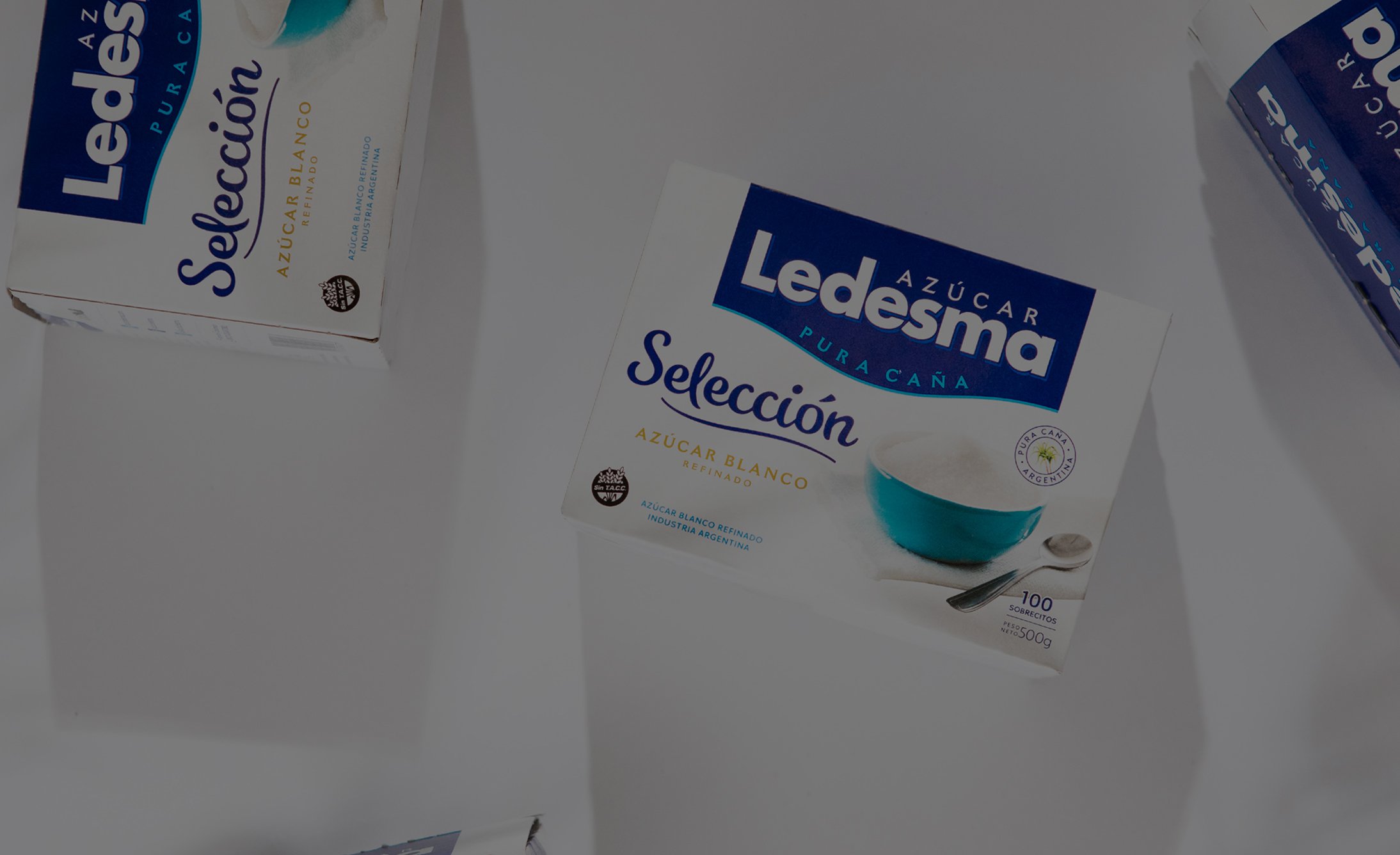 Boxes of Ledesma Azúcar sugar scattered on a white surface, featuring a prominent label with blue and white design, and a bowl of sugar graphic.