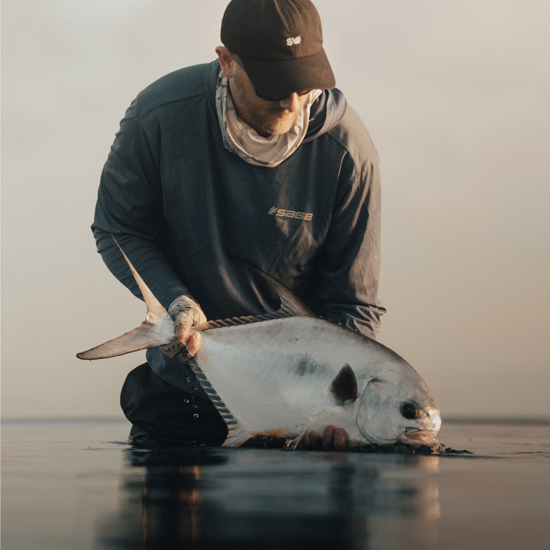 Saltwater angler holding a permit just above the water on a slicked out calm flat in Belize