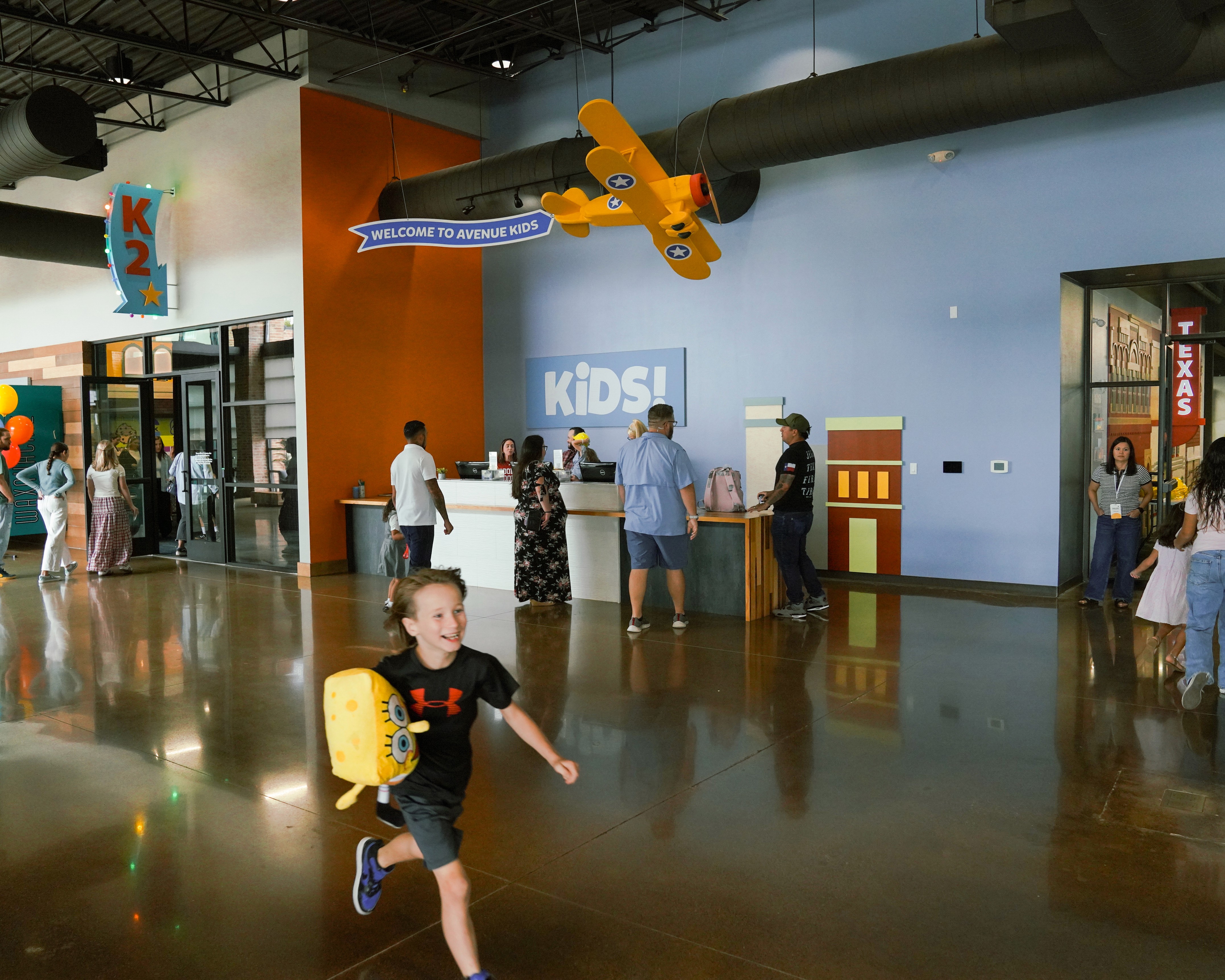 A busy indoor space with people walking around and a child playing, reflecting vibrant activity and interaction.