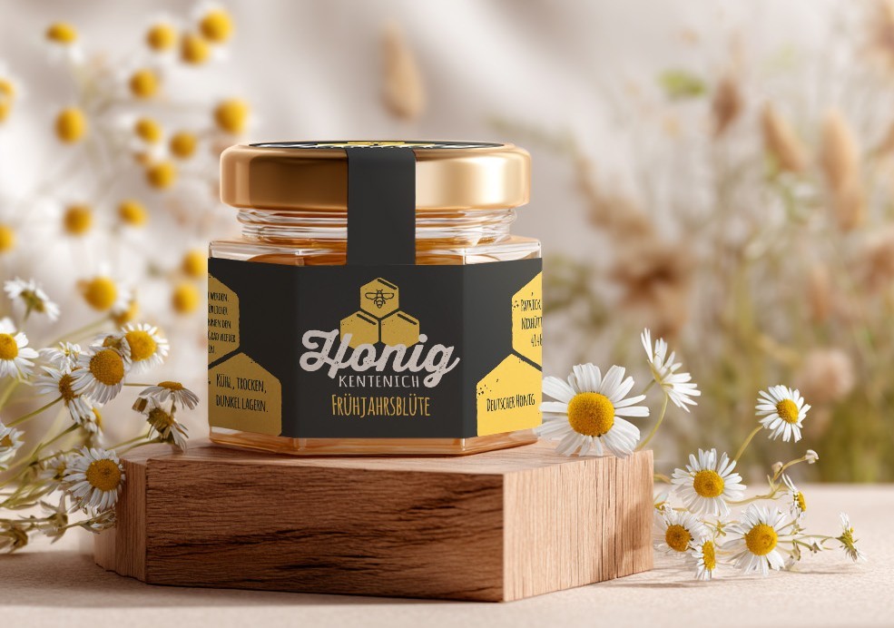 Detailaufnahme eines Honigglases mit modernem Etikettendesign für die Sorte Frühjahrsblüte, stilvoll inszeniert mit Holzpodest und Kamillenblüten. Professionelles Packaging Design für Honig Kentenich