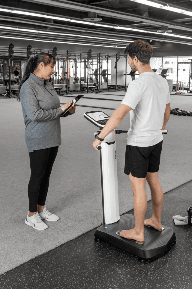 A fitness professional using a tablet to review body composition data with a client standing on an InBody professional body composition analyzer in a gym.