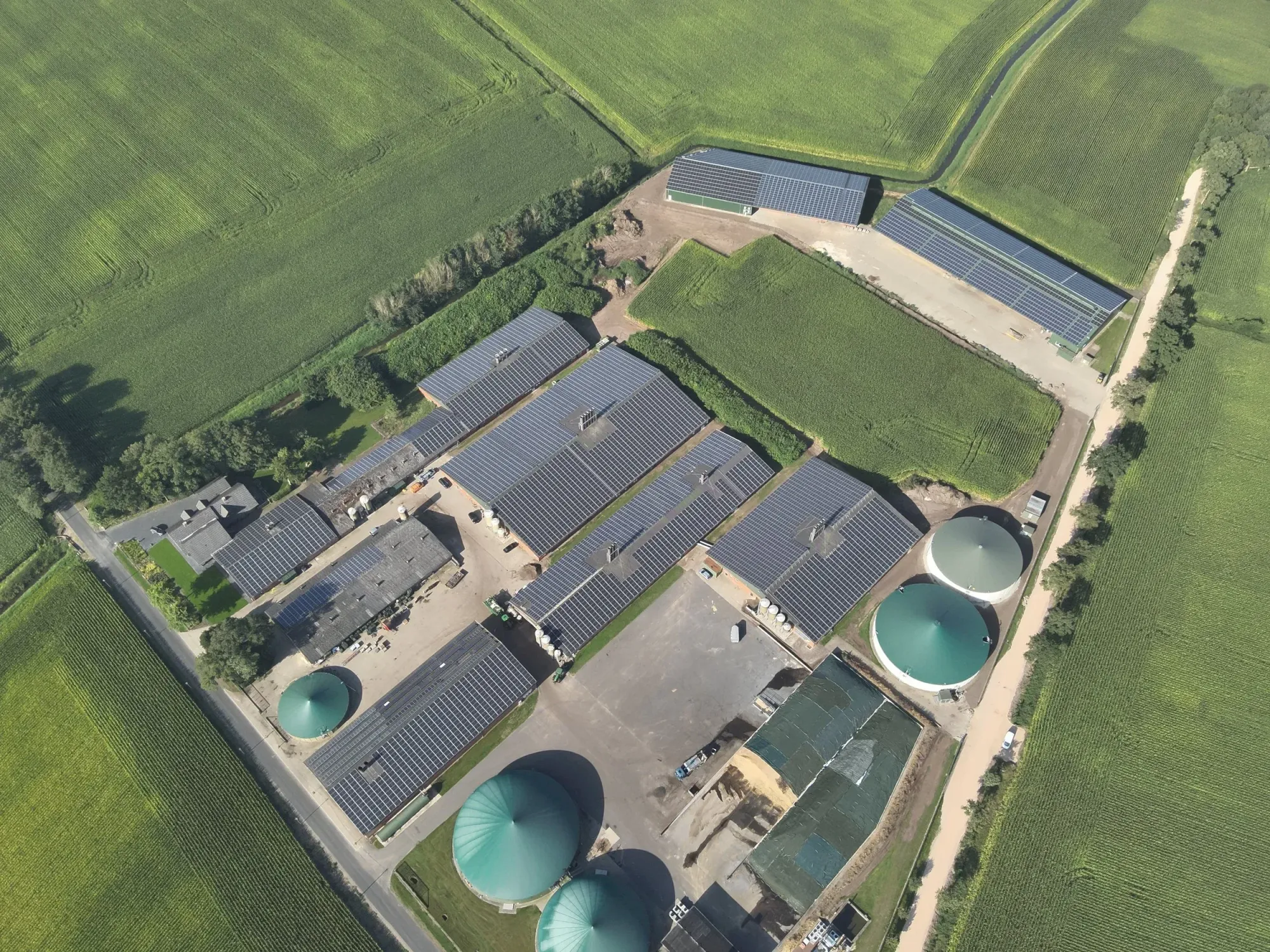 Luftaufnahme eines Bauernhofs mit Biogasanlage und Solarpanelen auf den Dächern.