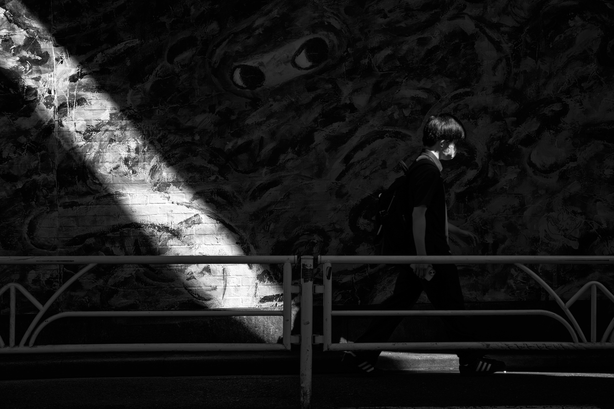 Black and white photograph looking down an escalator with a silhouette of a person walking in bright light at the bottom of the frame.