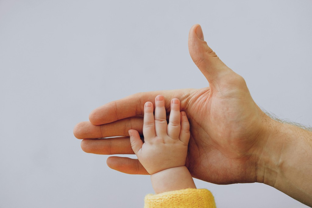 Infant's hand grasping adult's hand.