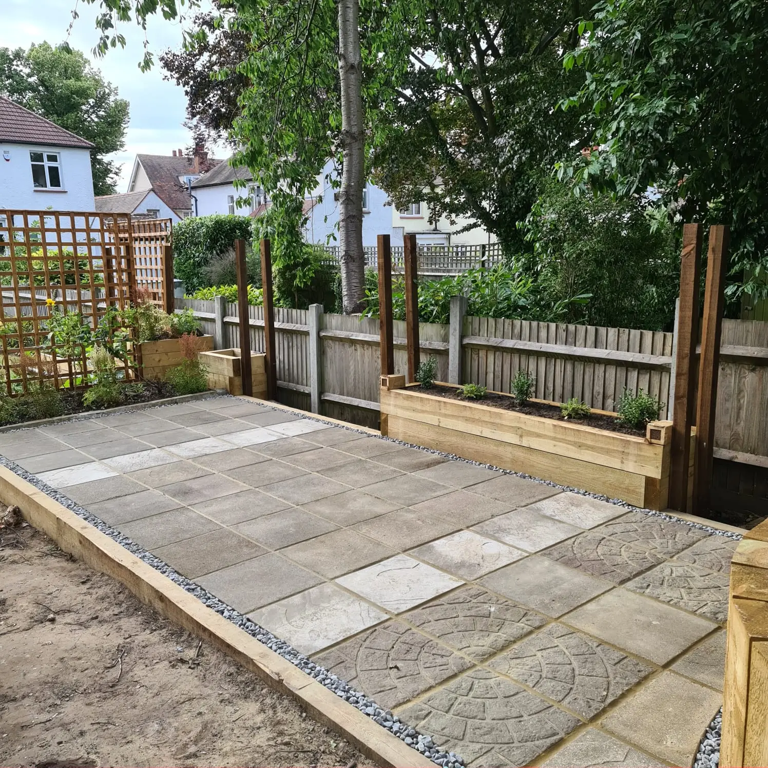 A freshly laid stone patio with wooden posts and a green garden backdrop.