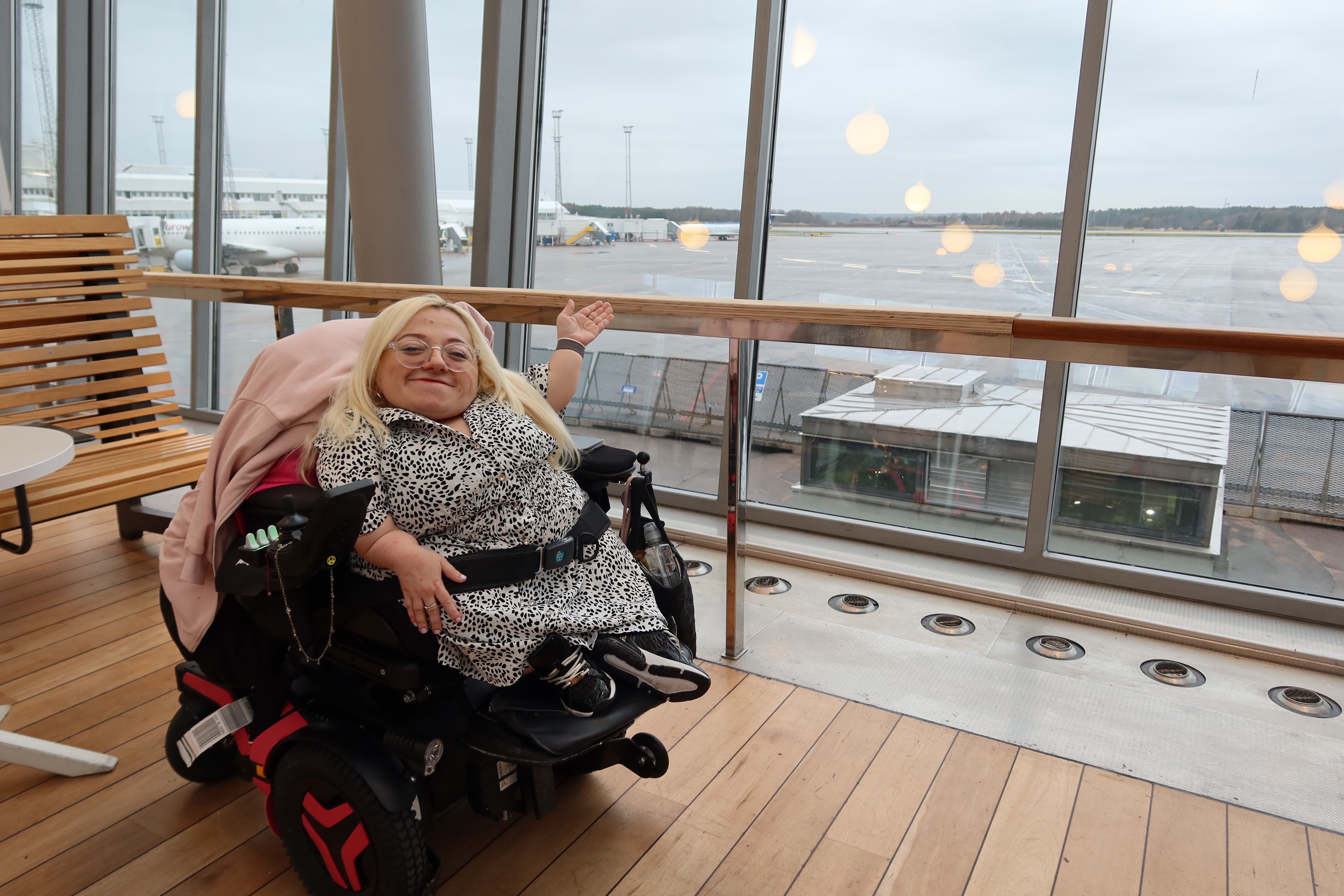 Gem in wheelchair pointing outside airport window