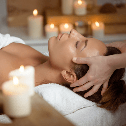 A person lying down at a spa getting a head massage with candles in the background