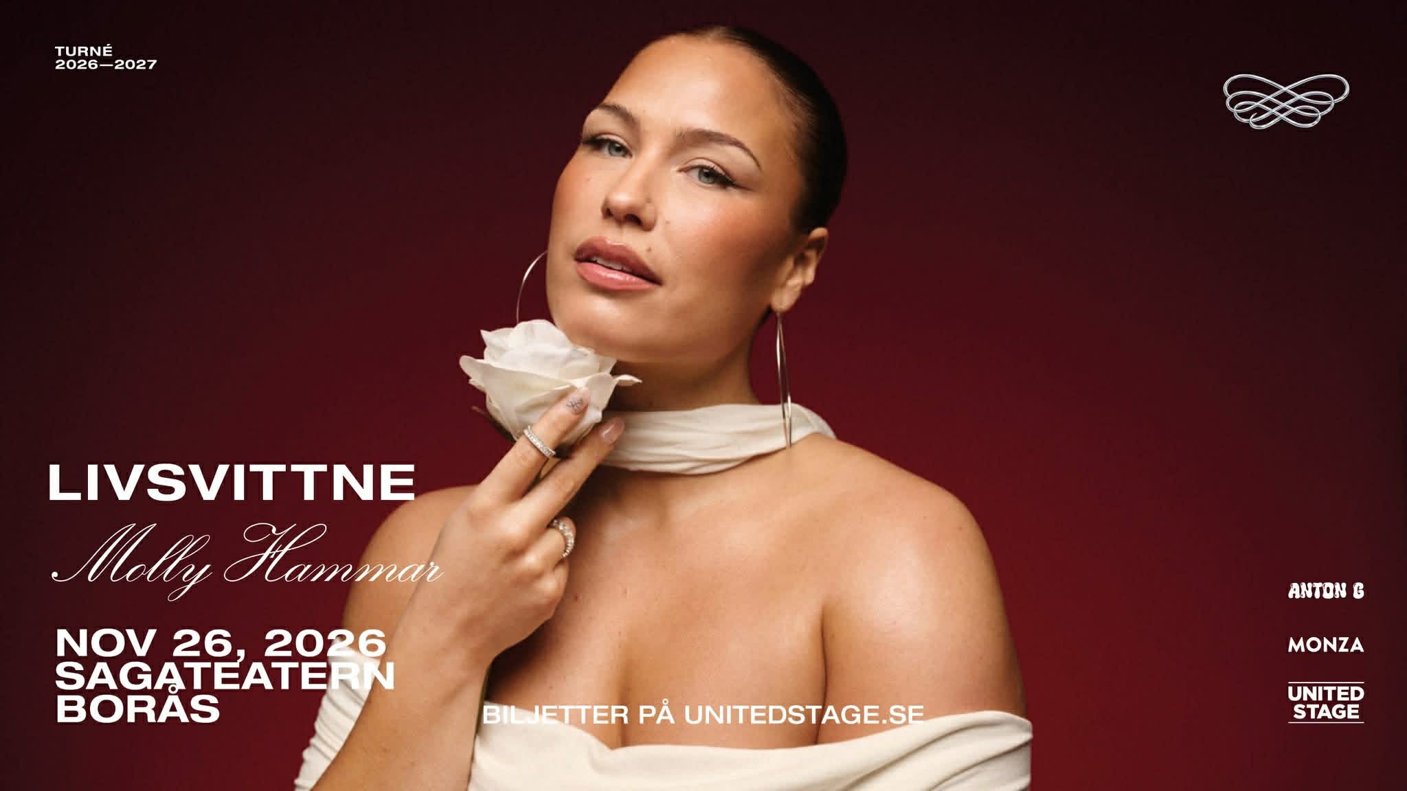 A young person with curly hair smiles at the camera while sitting in front of a laptop against a dark background.
