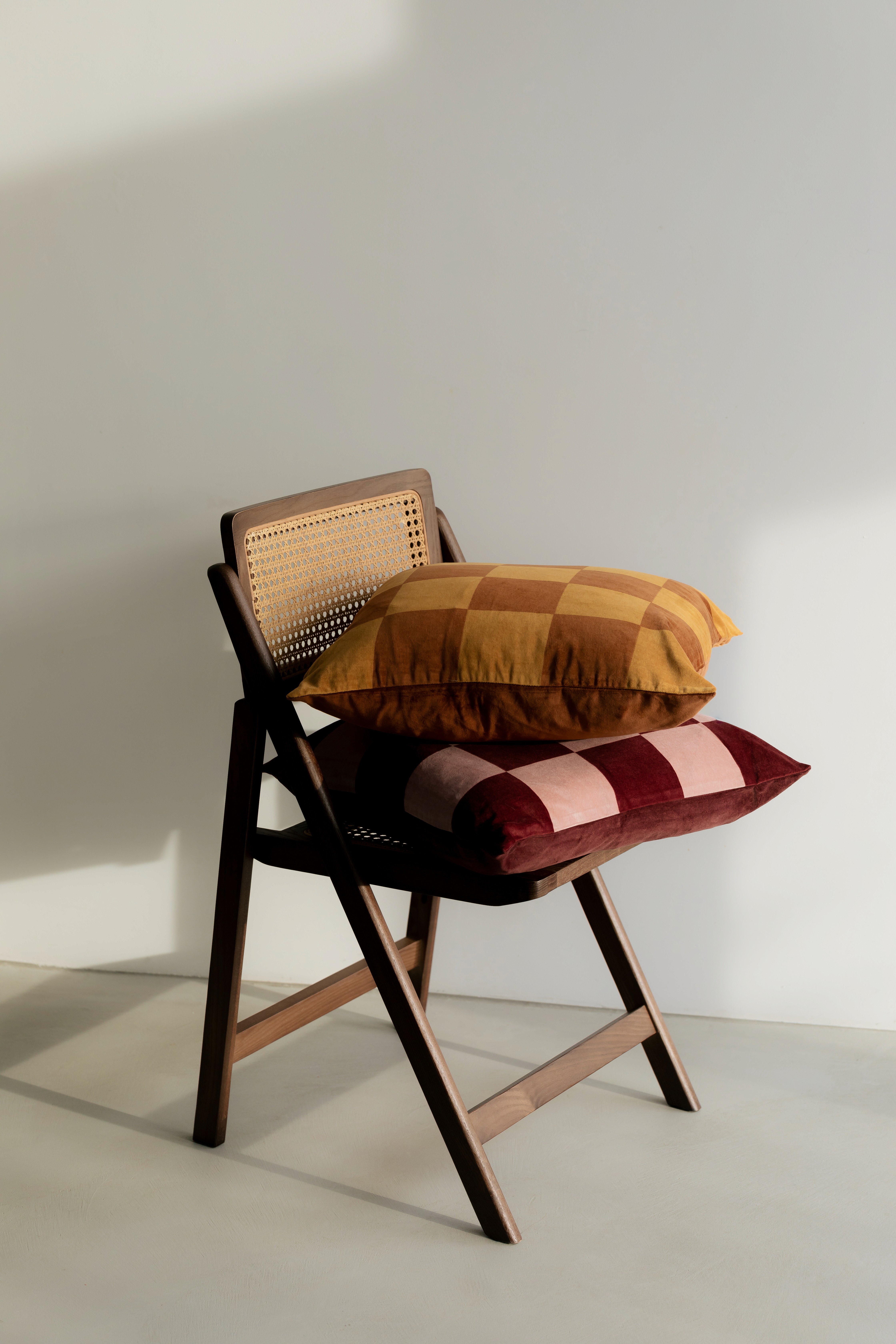 Edler Korbstuhl mit zwei karierten dicken Kissen auf der Sitzfläche vor hellem Hintergrund