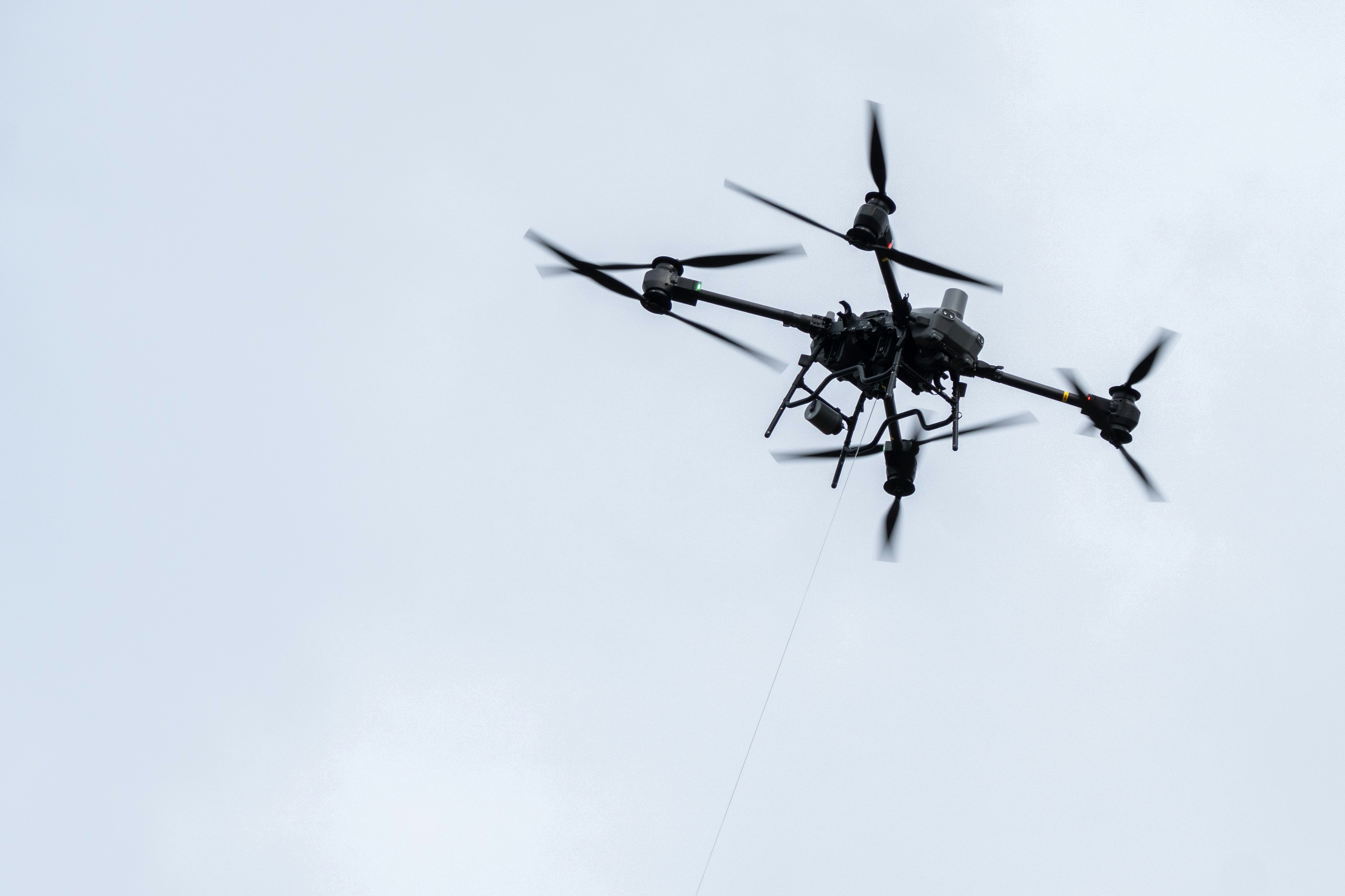 A drone flies high against a cloudy sky.