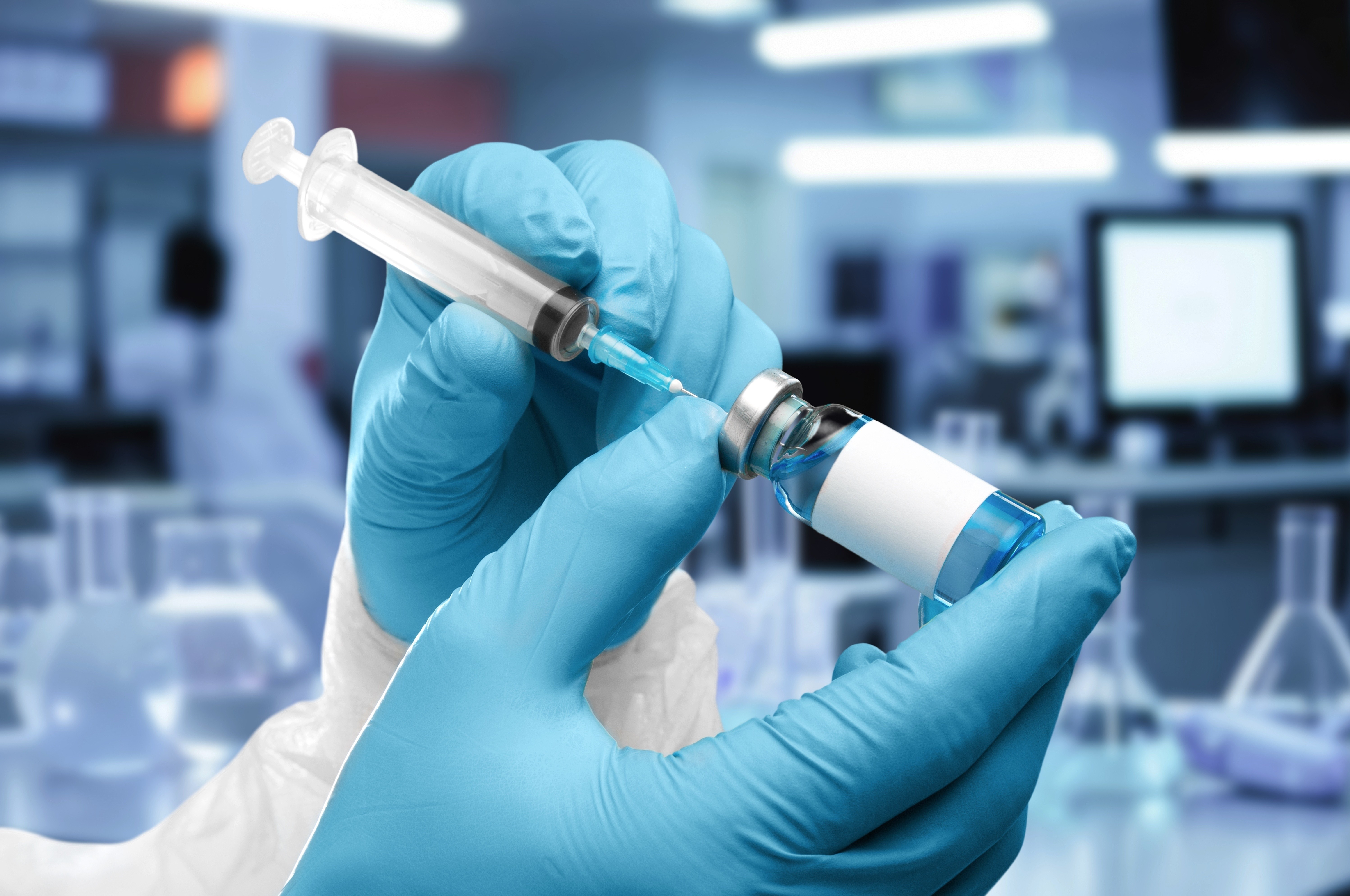 Gloved hands drawing blue liquid from a small vial into a syringe in a laboratory