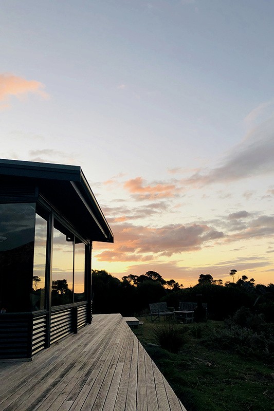 The dark-clad corner of the house and its timber deck at sunset