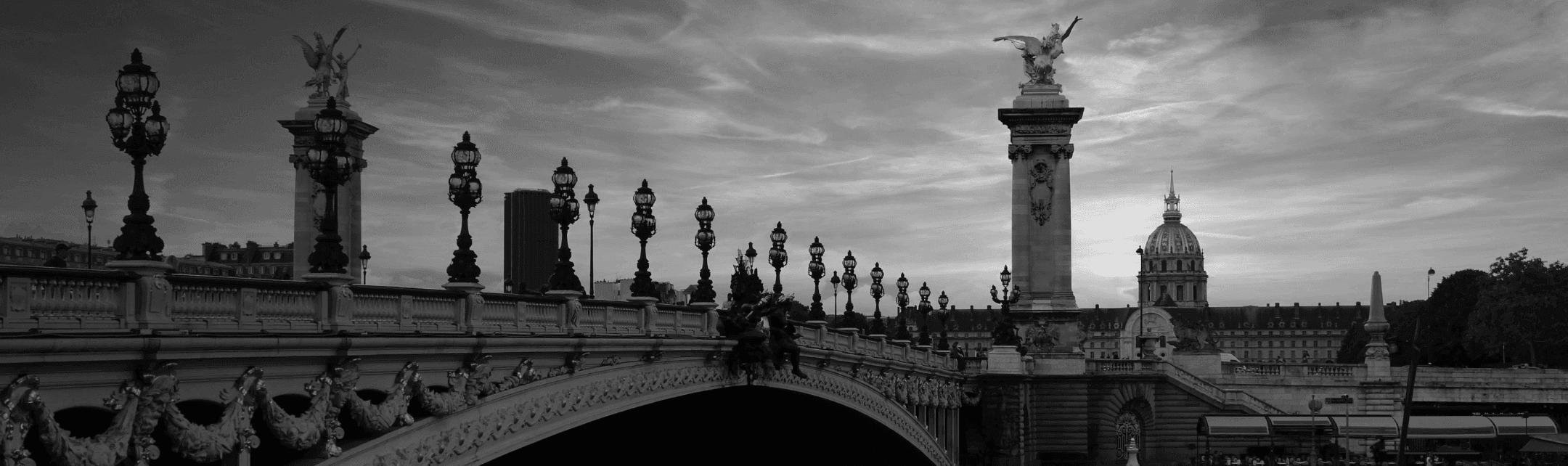 Black and white photo of Pont Alexandre III in Paris, France. Two people walk across the bridge.