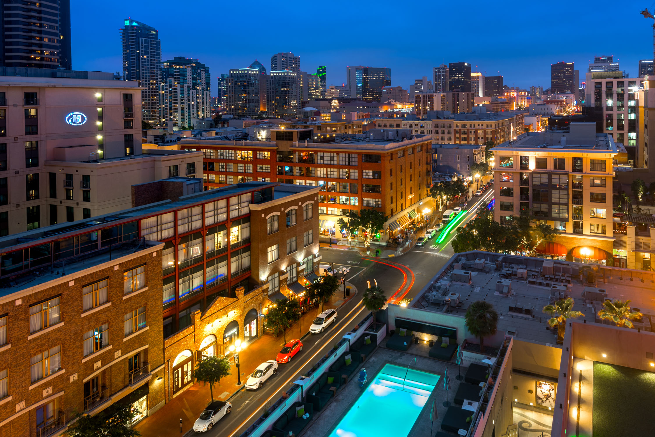 A twilight cityscape features a modern brick building with glowing windows and a lit swimming pool in the foreground.