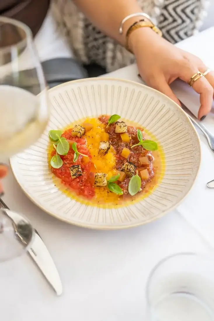 Colourful heirloom tomato starter with basil and croutons, plated at Annata Restaurant beside a glass of white wine