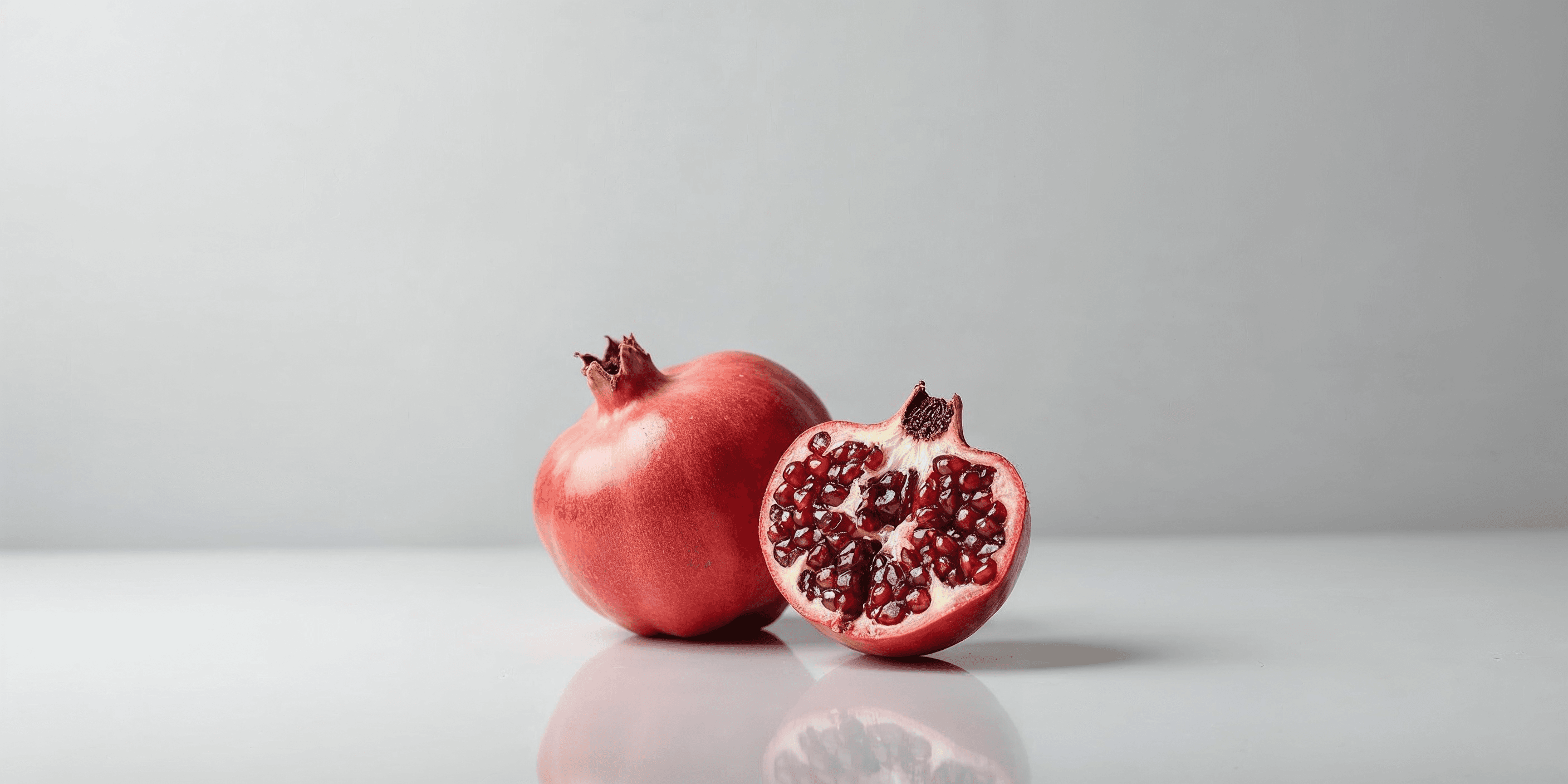 whole and cut-open pomegranate on a smooth white surface