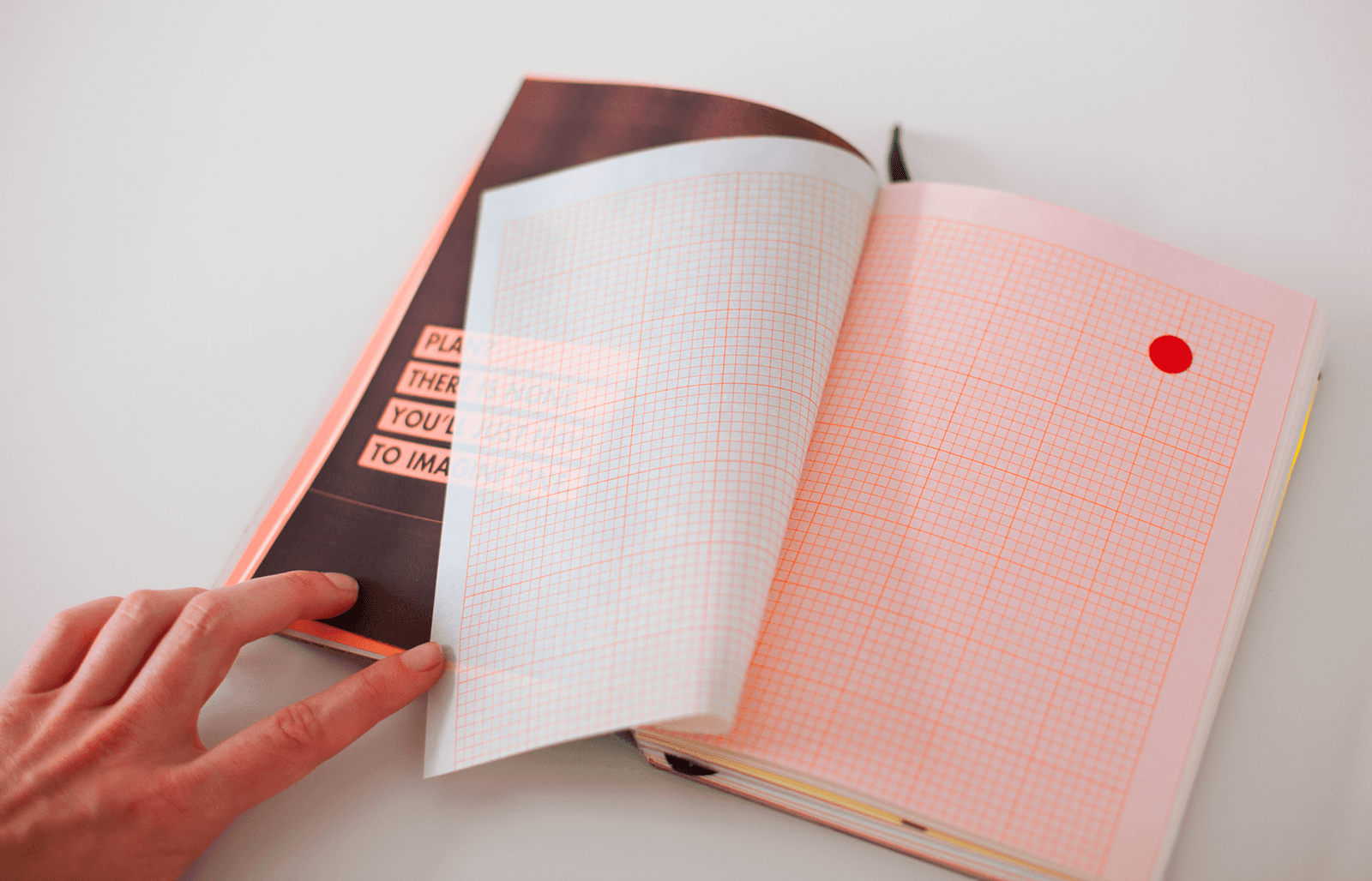 Spread open to pink risographed words with transparent page and white paper with pink grid lines. A red circle adorns the top right corner of the page