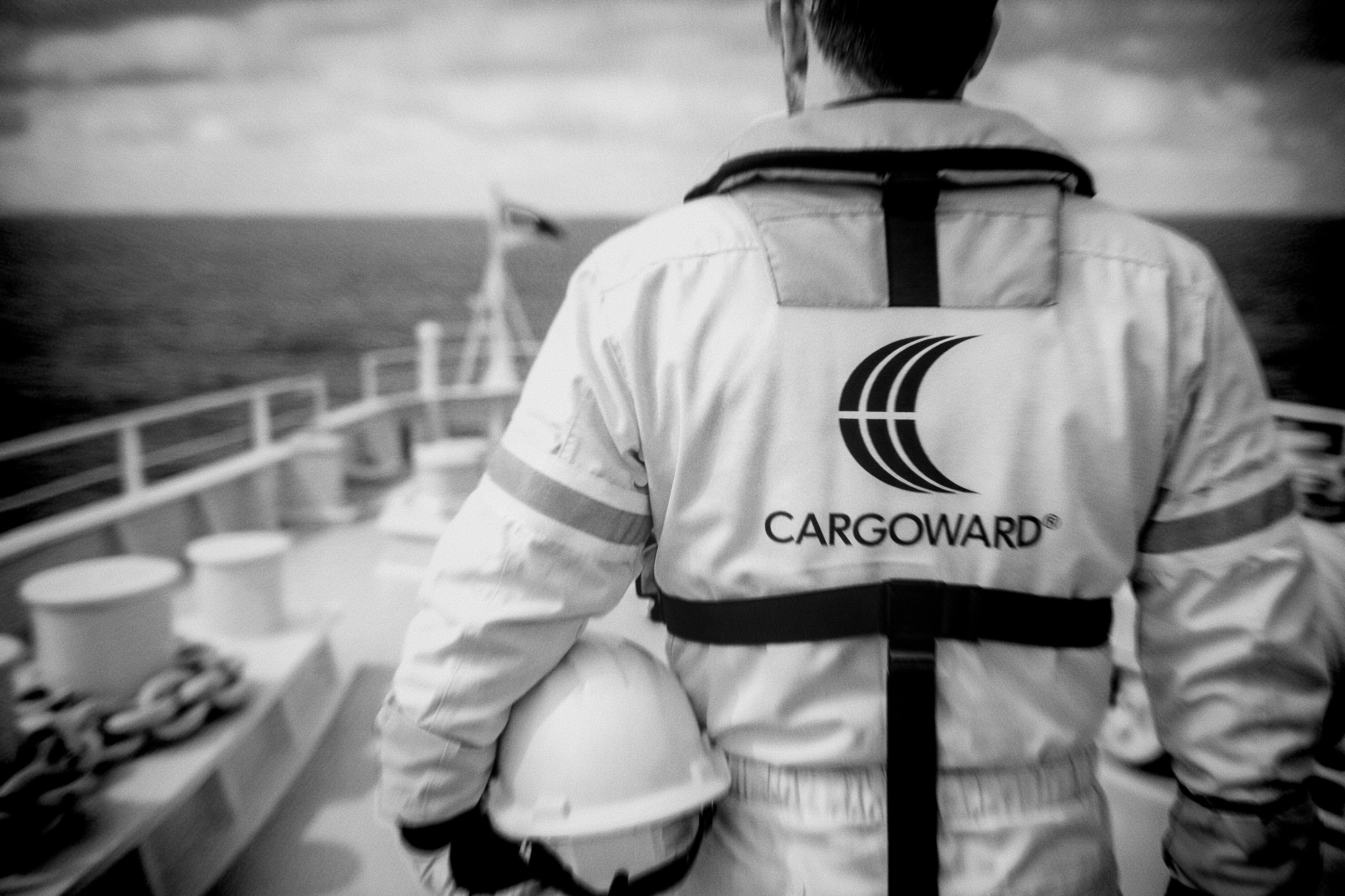 CARGOWARD® maritime professional on a vessel deck, wearing PPE and lifejacket, holding a hard hat and looking out to sea.