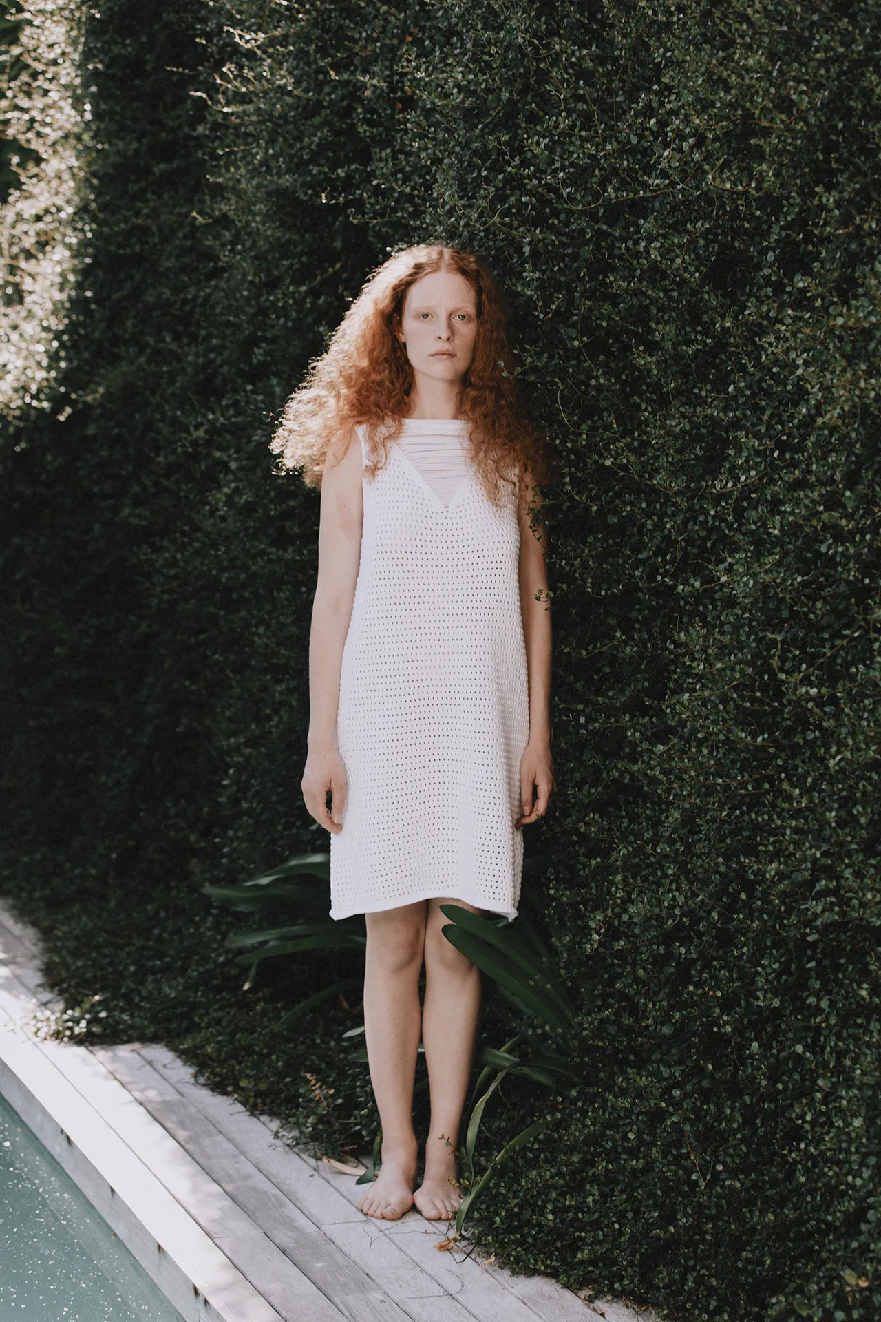 Annapurna SS26 collection white sleeveless crochet-knit dress worn by a model standing near a pool.
