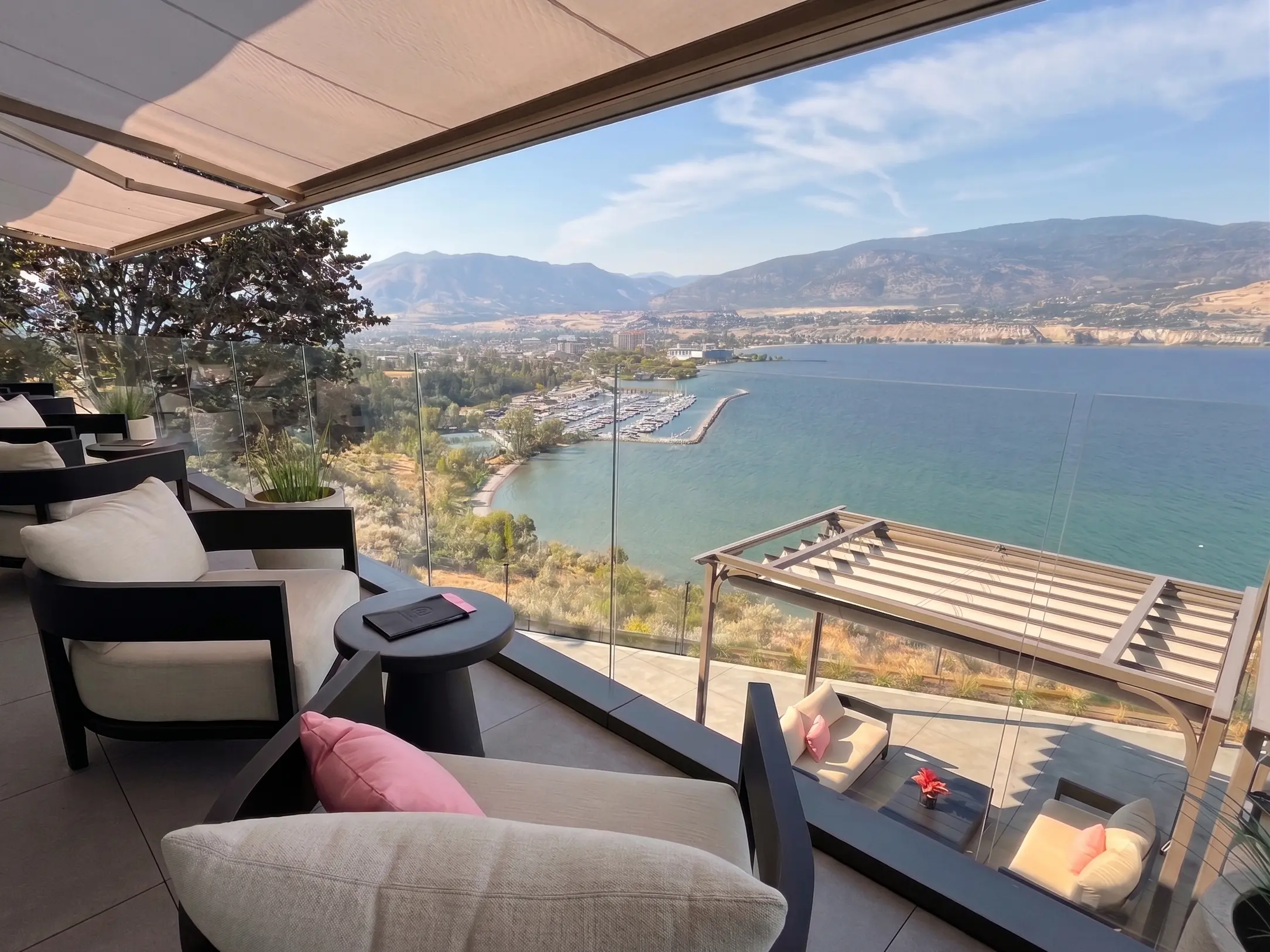 A luxurious commercial patio with modern lounge chairs overlooking a scenic waterfront, enclosed by a seamless, clear commercial glass railing system that provides an unobstructed panoramic view.