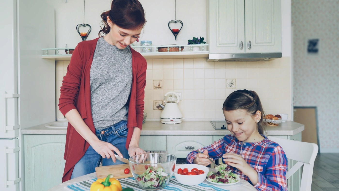 A mother serves a fresh salad to her daughter at the table, reflecting common mealtime and picky-eating concerns
