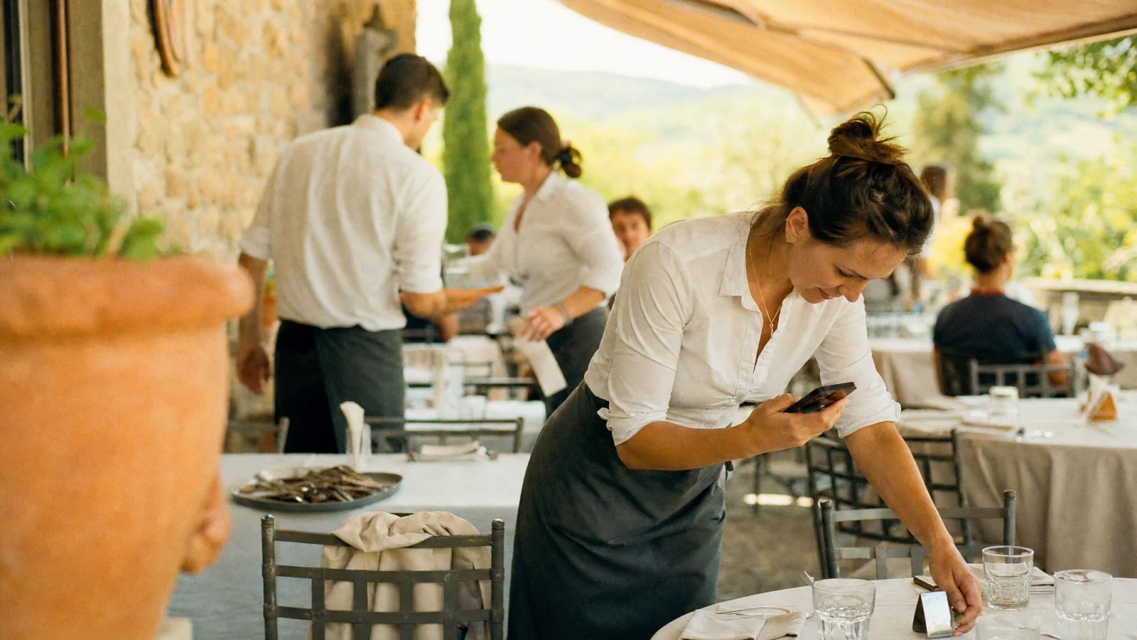 Cameriera prova la scansione del QR con il telefono su un tavolo della terrazza