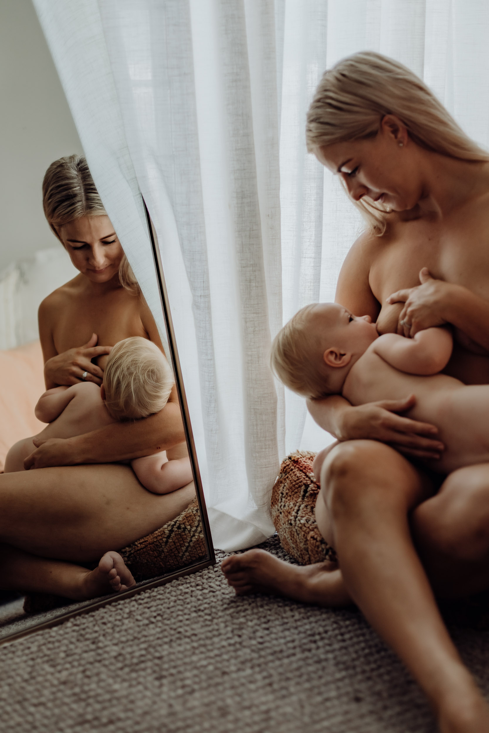 Breastfeeding mother holding her newborn in soft window light during a lifestyle motherhood session in Mackay.