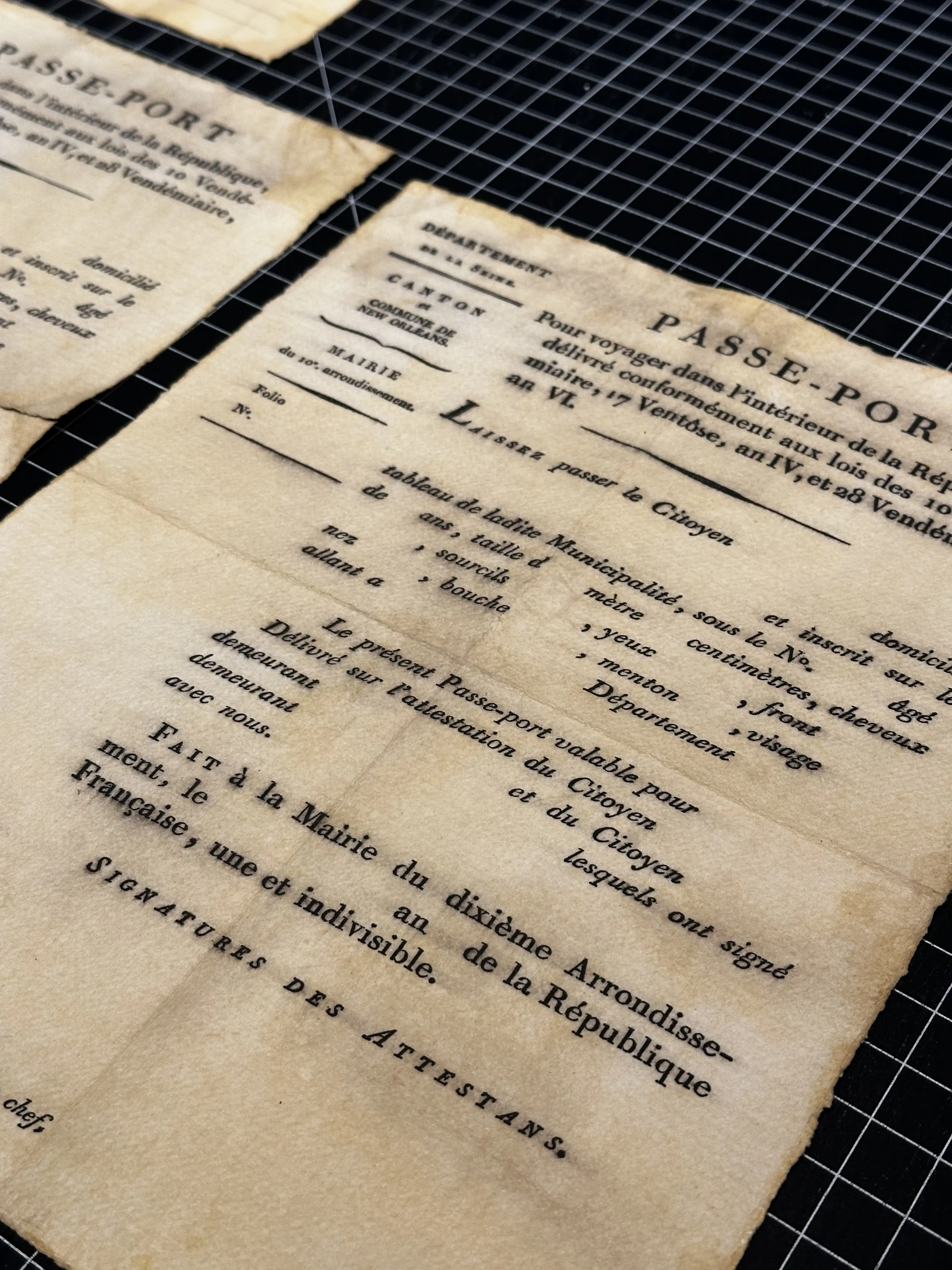 An old, weathered passport document lies on a black grid surface, showcasing intricate, vintage typography and faded ink that reflect historical design elements. Rob Harrigan Design. Rob Harrigan. 