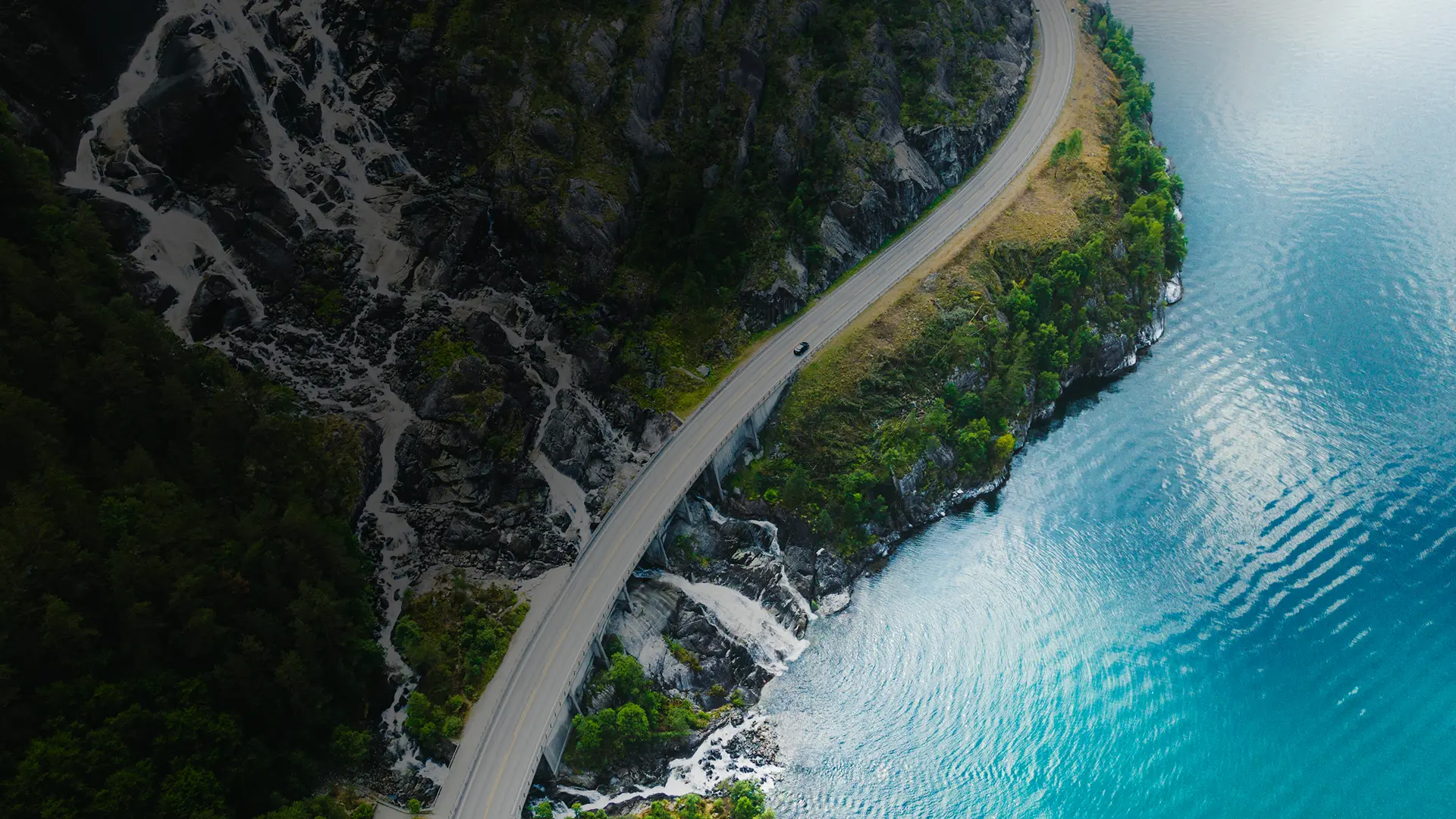 Aerial view of a truck driving along a winding coastal highway beside blue water, used on GIA Group, LLC’s Certificate of Insurance page to symbolize speed, reliability, and nationwide coverage.