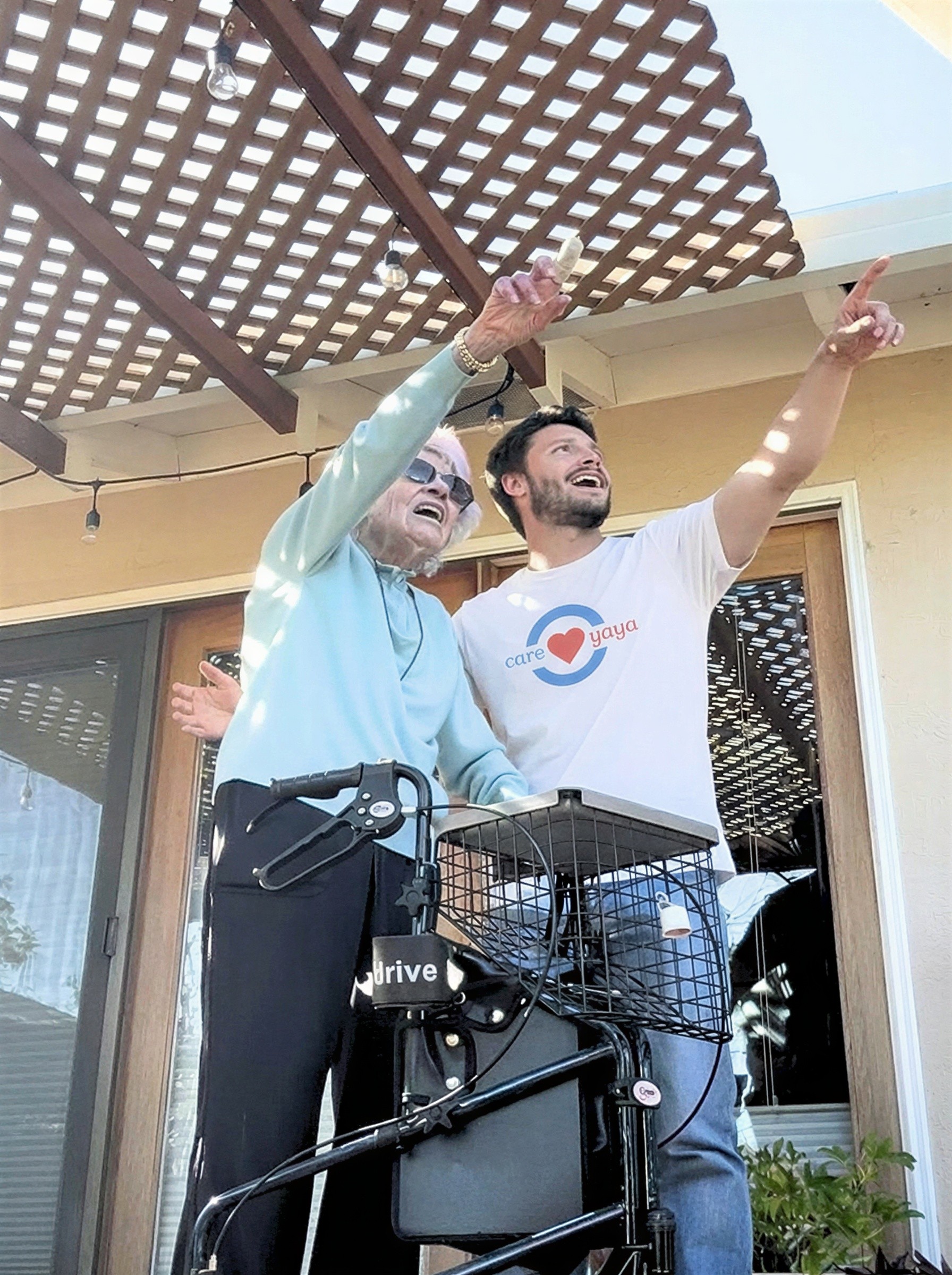 Older woman with walker stands with young man in CareYaya t-shirt. They point to something in the distance