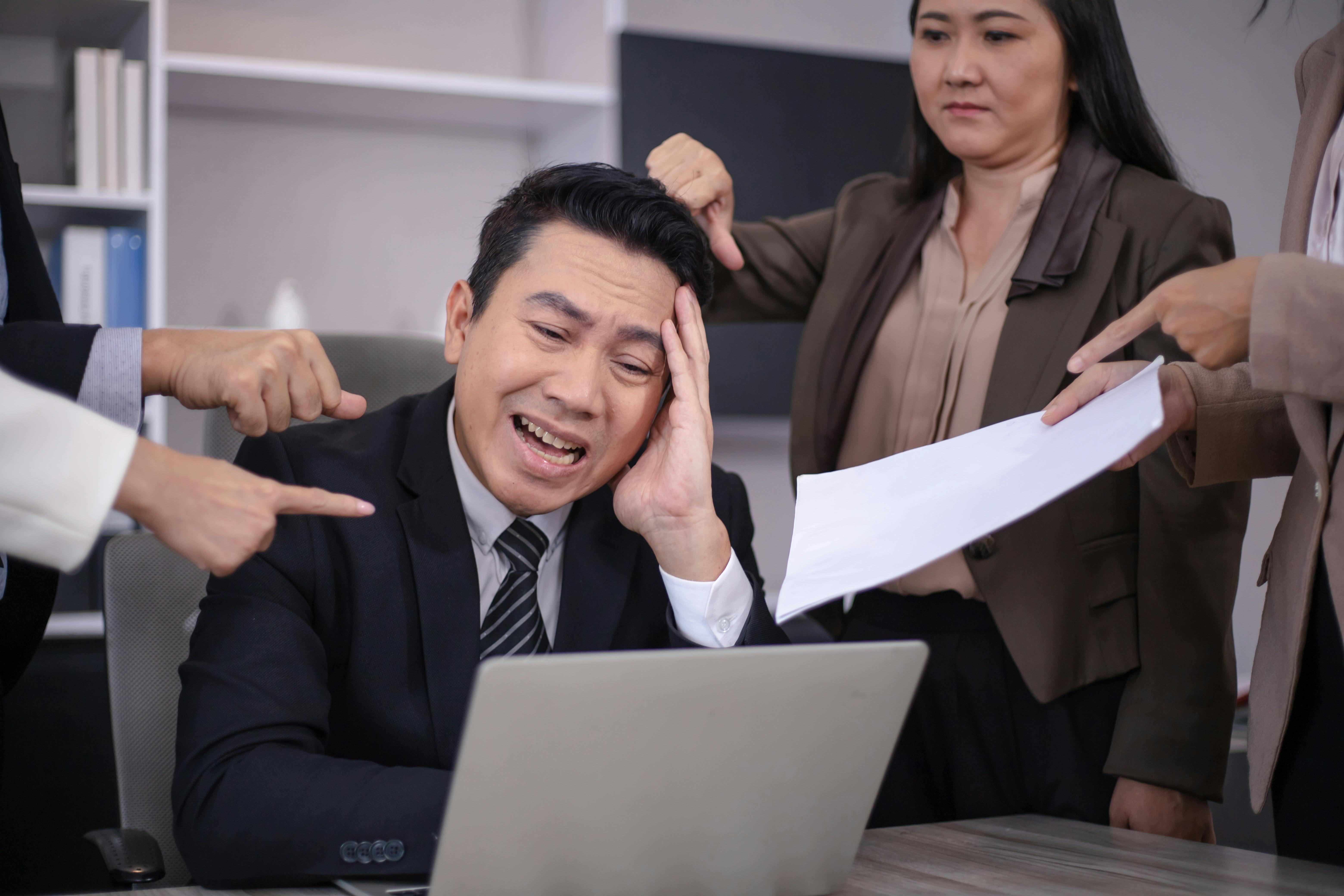 Stress broker looking at his laptop with lenders around him