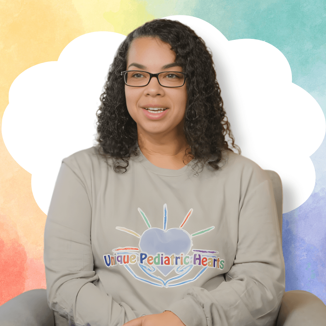 Nikki Estess, a nurse at UPH, talks to a camera off-screen in front of a watercolor background. She wears a grey sweatshirt with the company's logo on top.