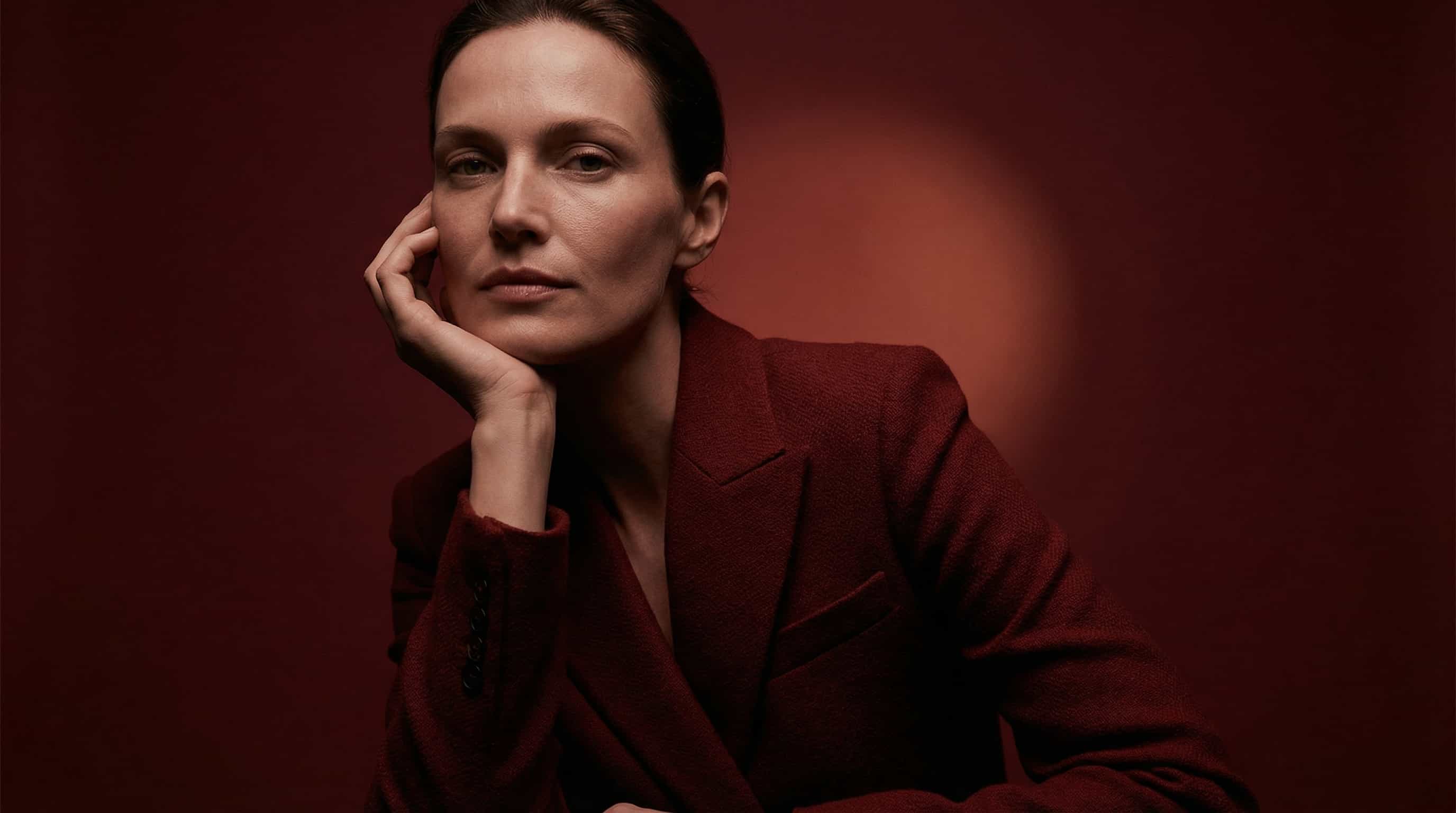 Woman in a red jacket with a calm expression on a red background.