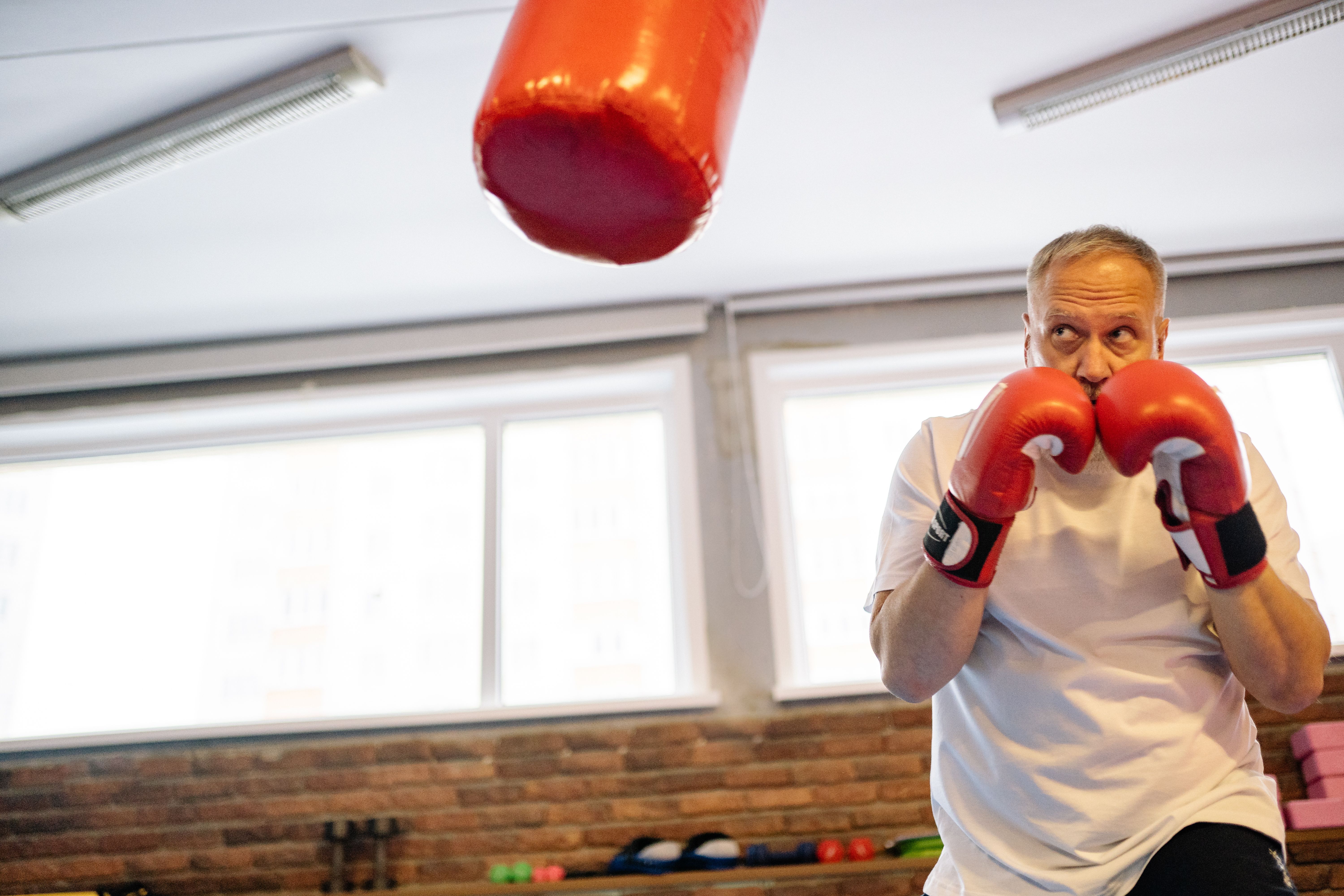 Older man in boxing gloves training on a heavy bag in a gym