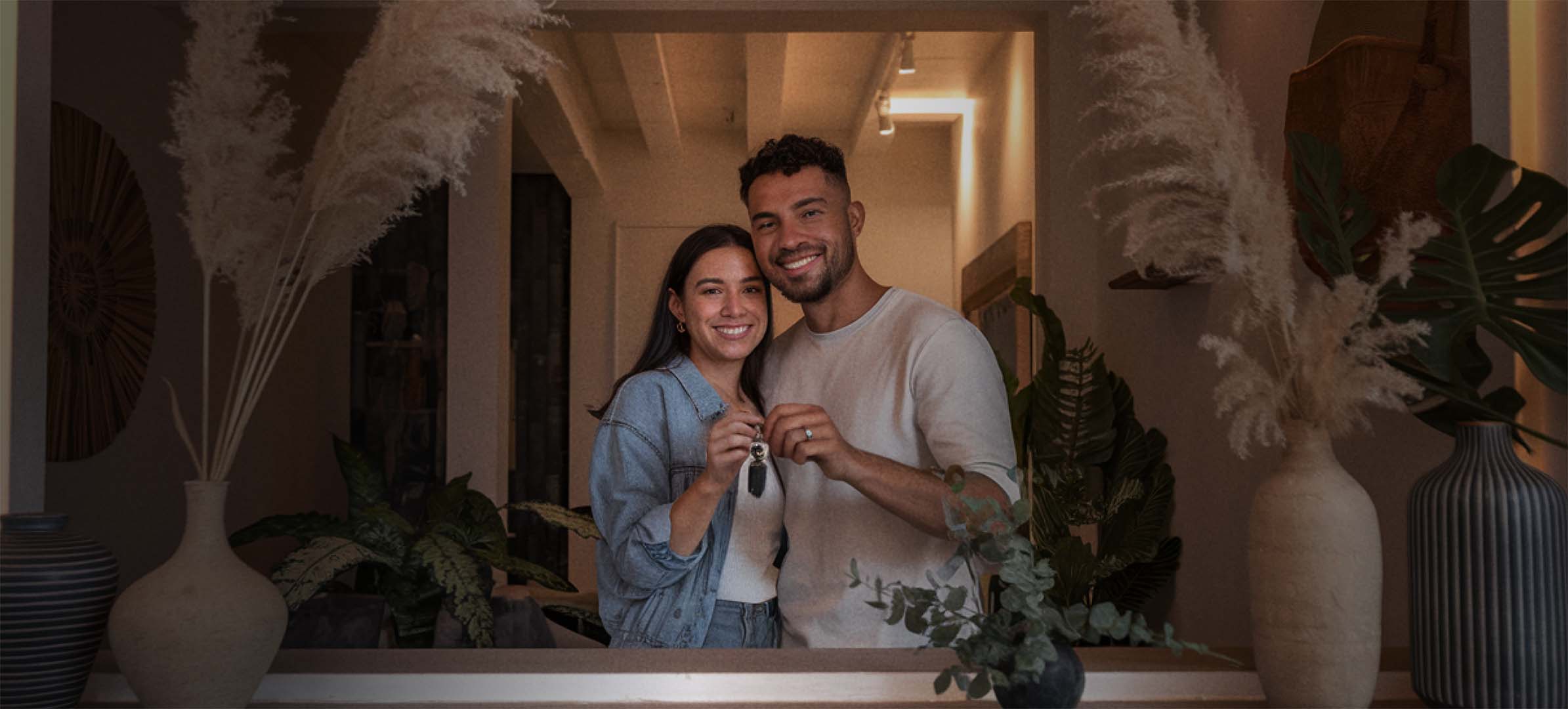 Casal sorrindo segurando chaves dentro de uma casa bem iluminada.