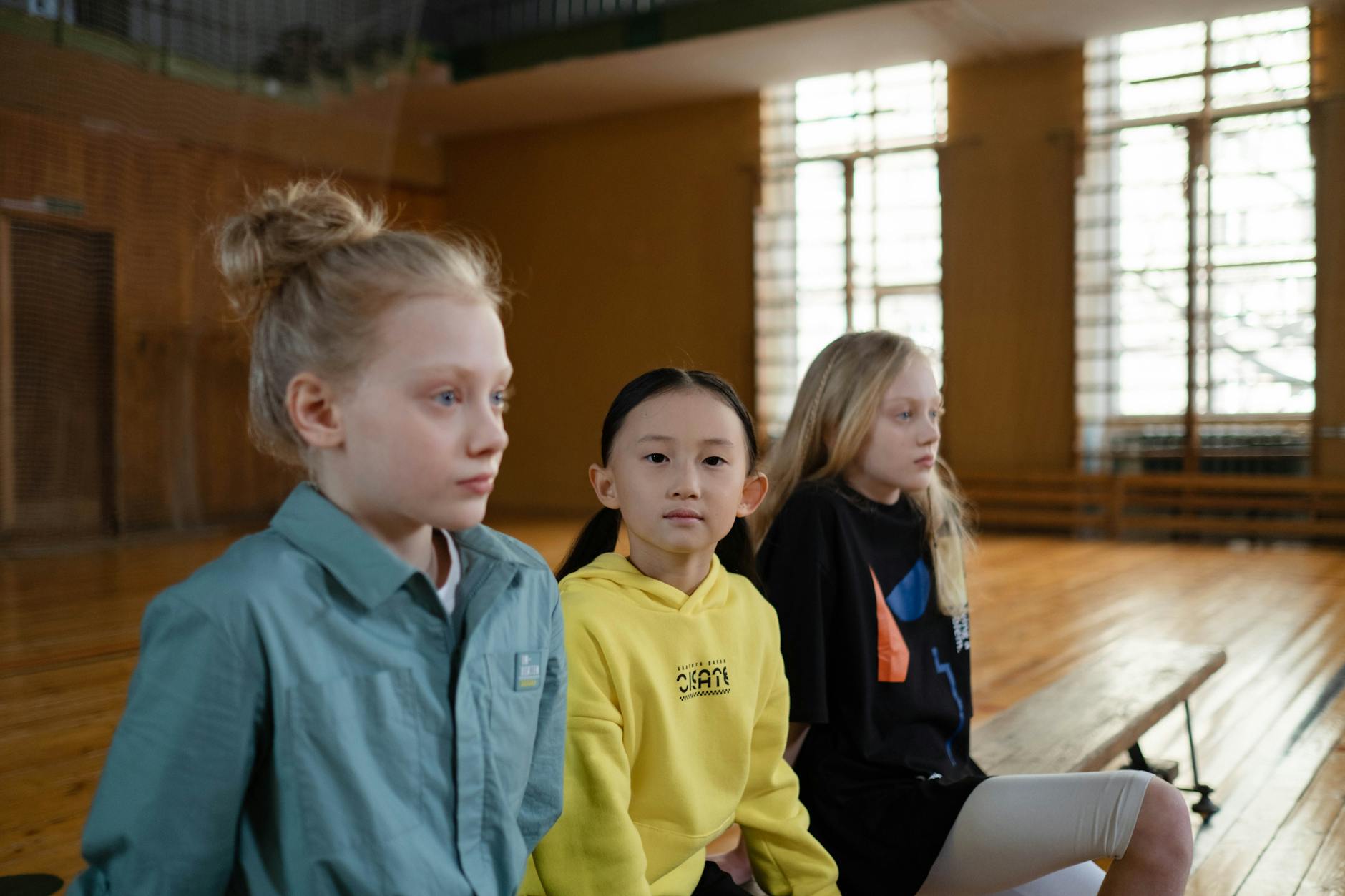 Students sitting in organized rows on a polished gym floor listening to instructions during a transition.