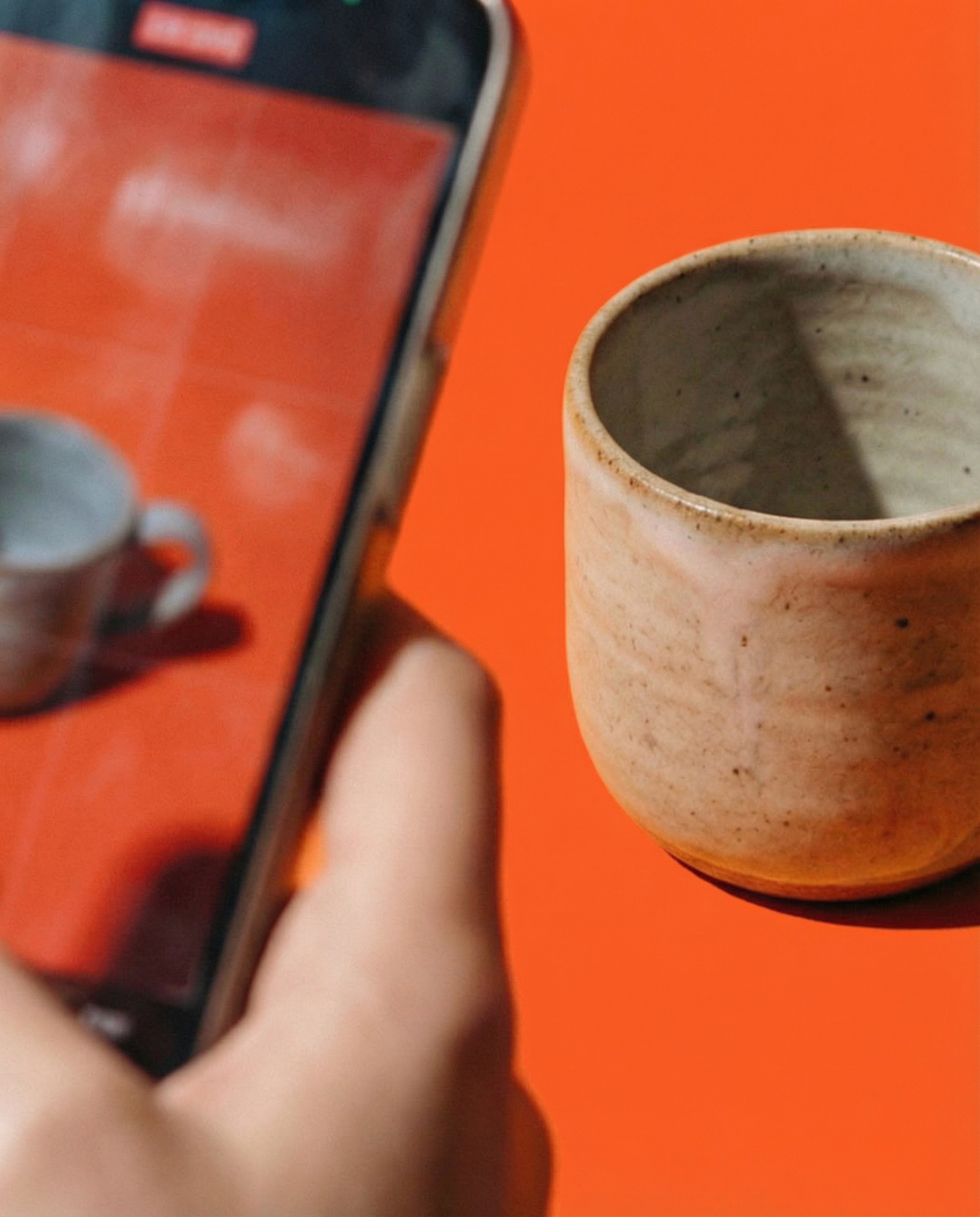 Hand holding phone next to ceramic cup